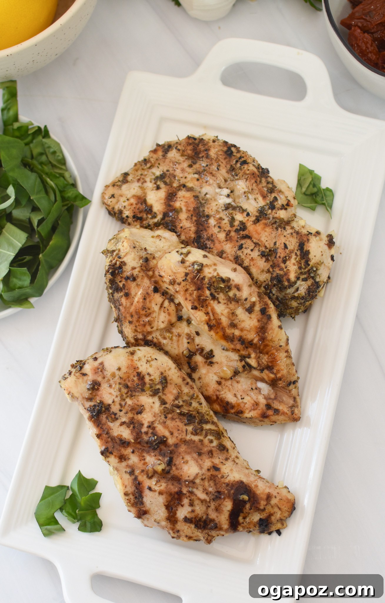 Copycat Carrabba's Chicken Bryan 7 Grilled chicken breasts resting on a white plate, ready for topping.