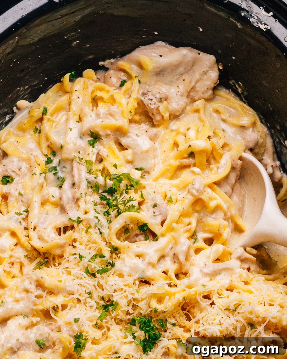 Creamy Slow Cooker Chicken Alfredo 10 Close-up shot of creamy Crockpot Chicken Alfredo with a spoon lifting pasta and chicken.