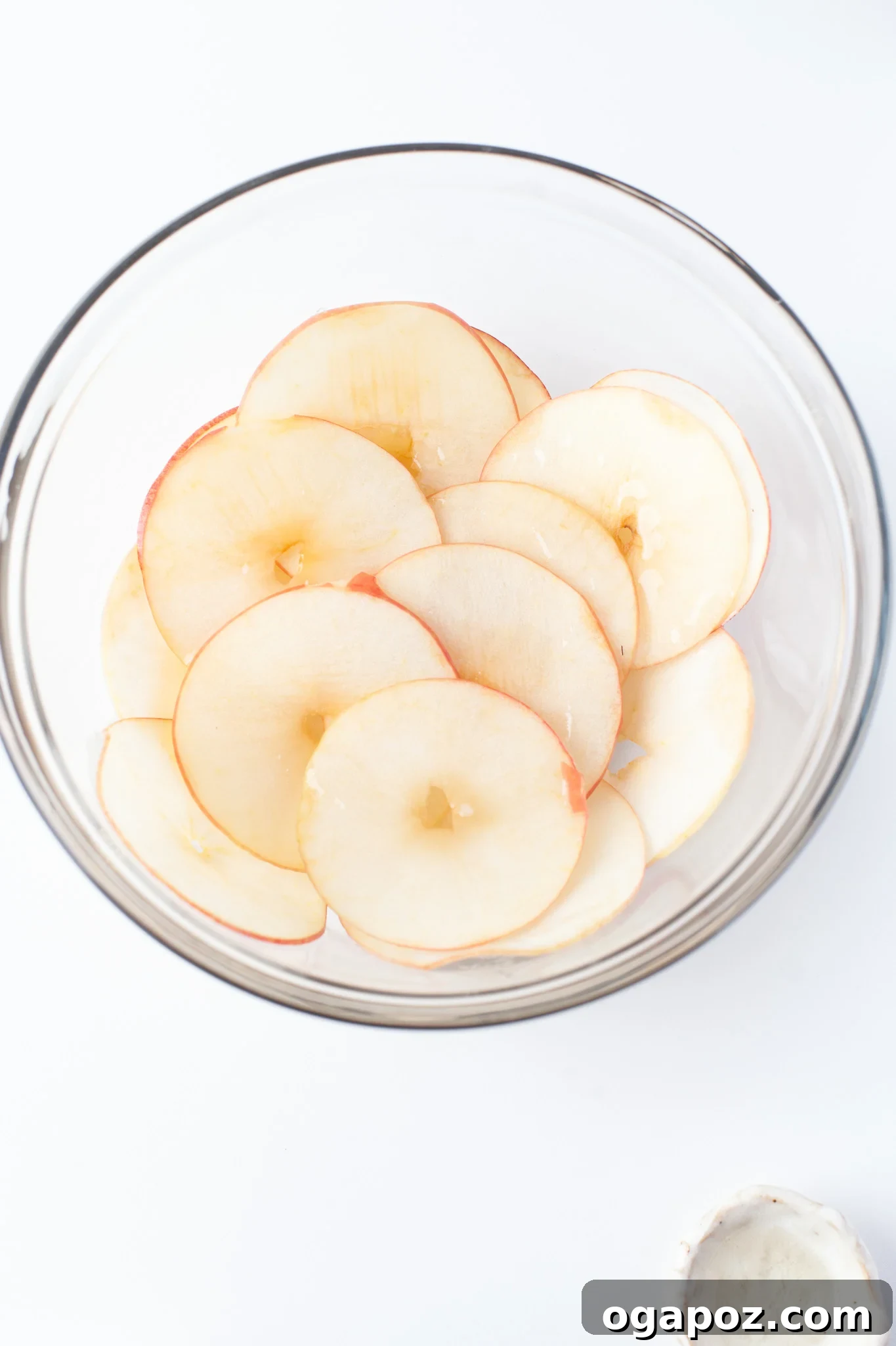 Simple Air Fryer Apple Crisps 6 Thinly sliced apples being gently tossed with melted coconut oil in a clear mixing bowl, preparing them for spice application.