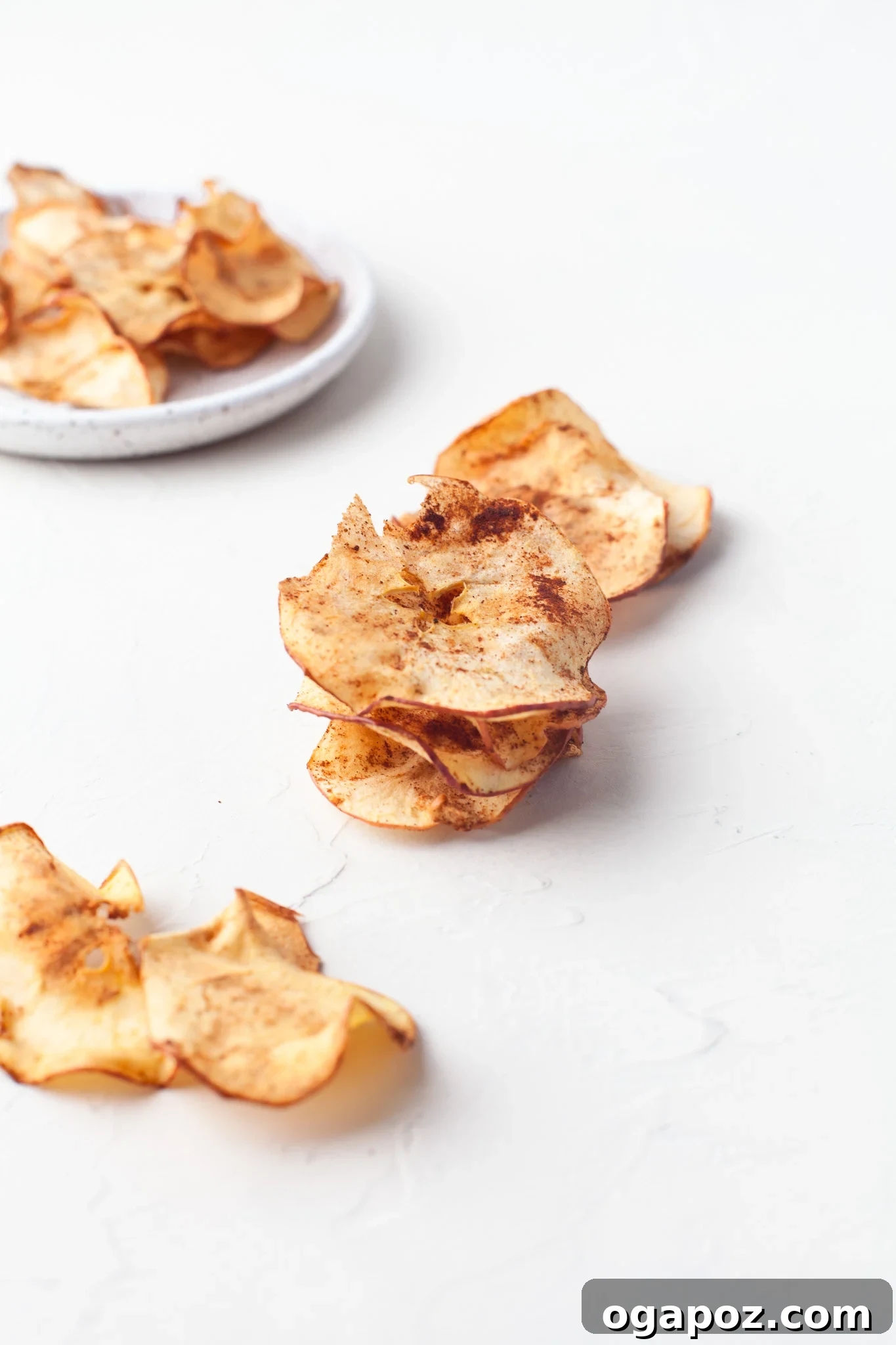 Simple Air Fryer Apple Crisps 9 An inviting display of freshly made Air Fryer Apple Chips casually spread across a rustic white table, ready to be sampled.