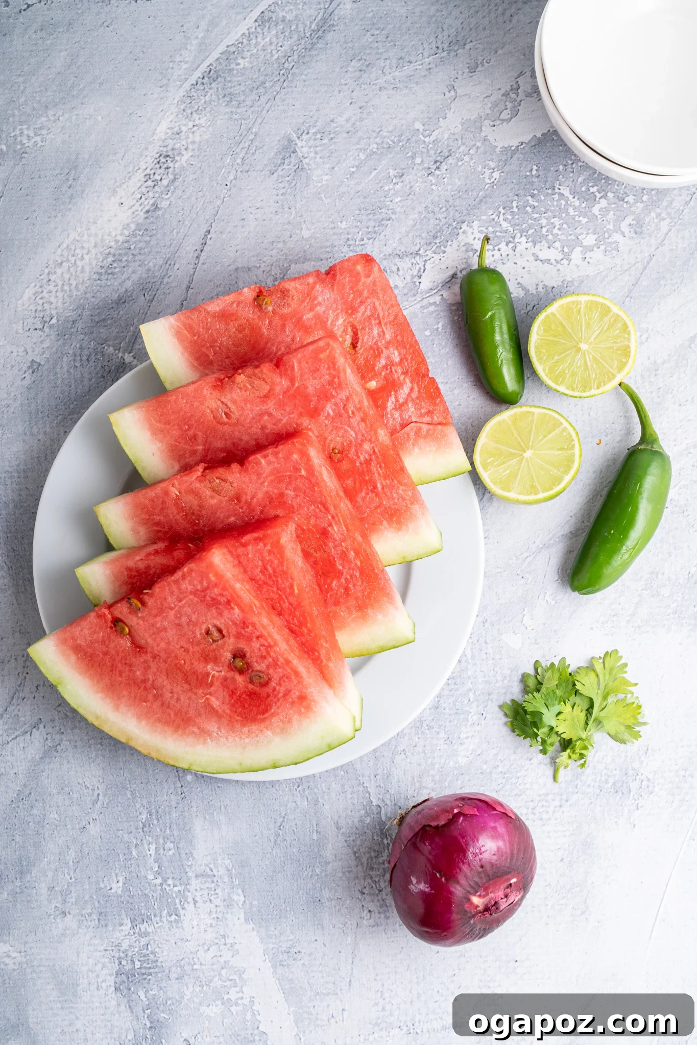 Summer Watermelon Salsa 4 Ingredients for Easy Watermelon Salsa on a blue cutting board, including diced watermelon, red onion, jalapeño, cilantro, and limes.