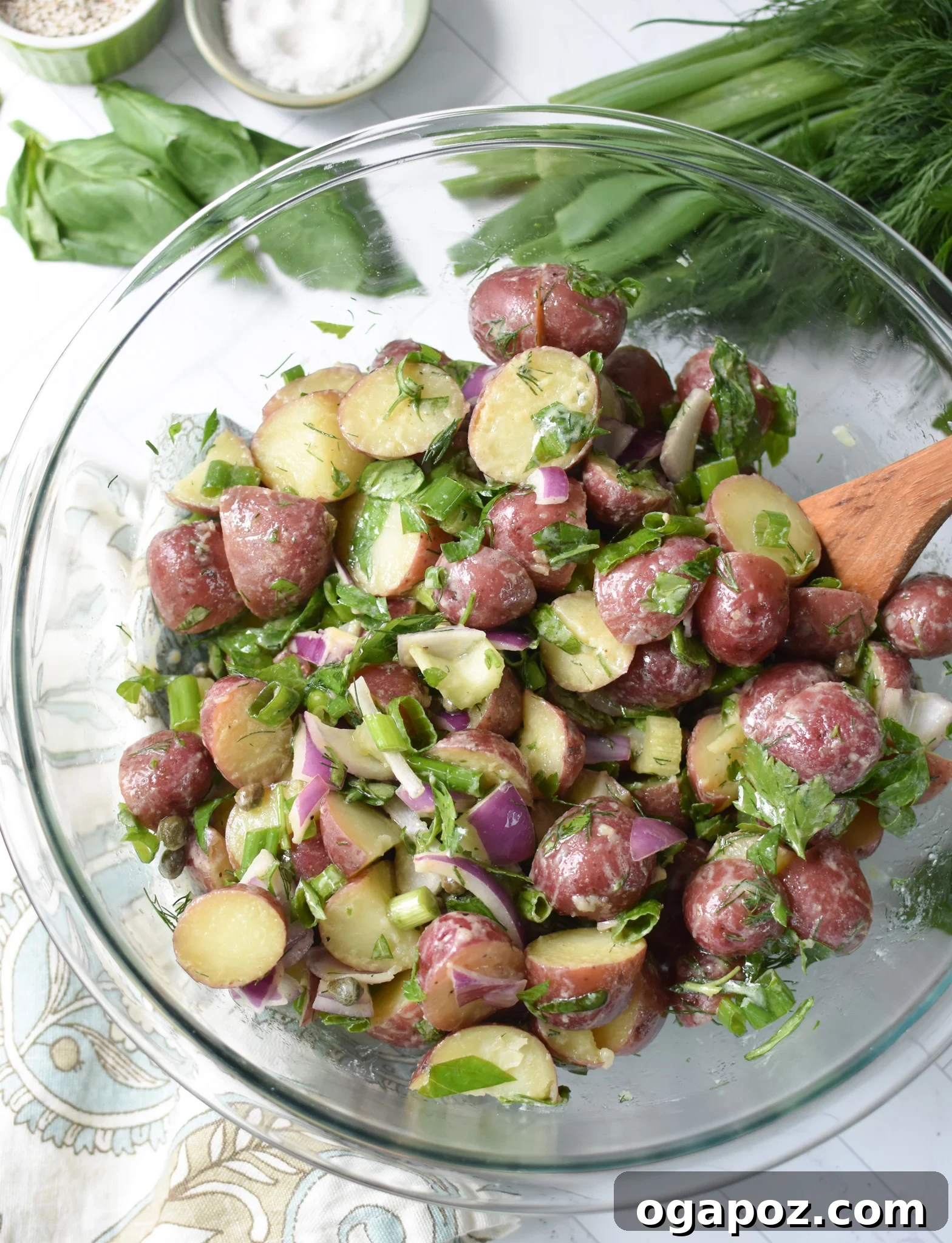 Bright and Tangy Potato Salad 12 No Mayo Potato Salad being tossed with dressing in a glass bowl using a spoon.