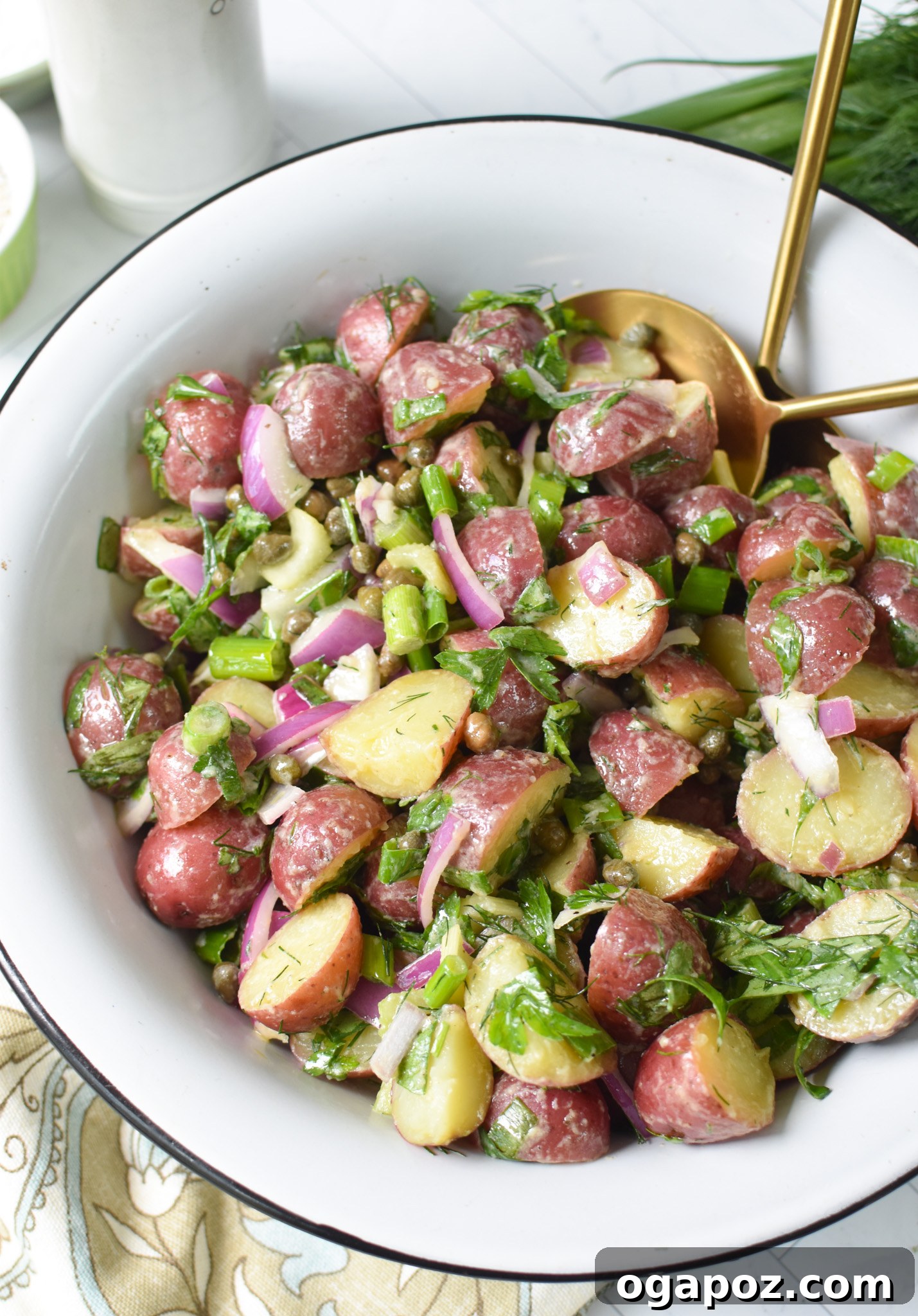 Bright and Tangy Potato Salad 13 No Mayo Potato Salad in a white bowl with a black rim, ready to be served with gold spoons.