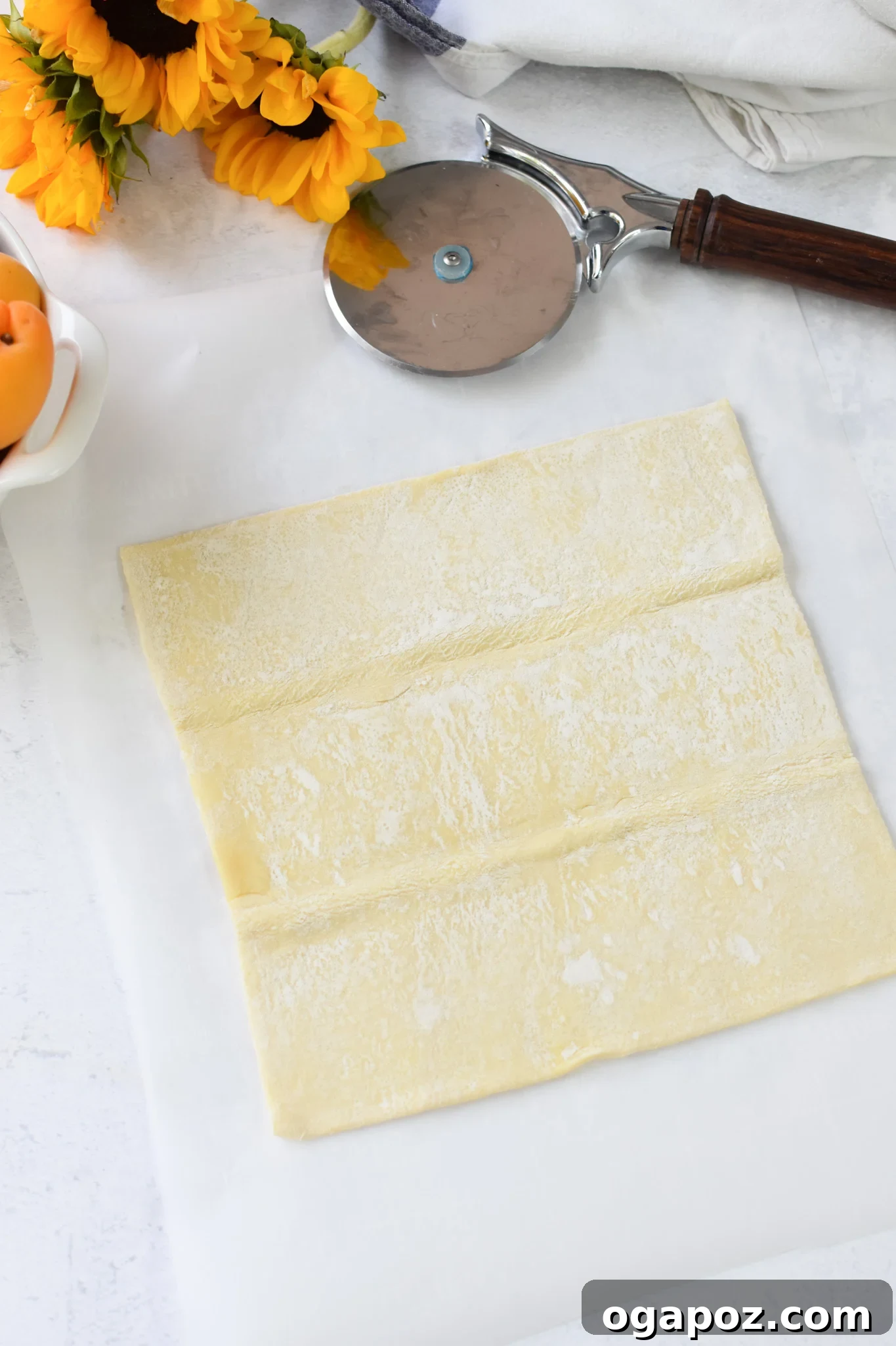 Effortless Golden Peach Tart 5 A thawed sheet of puff pastry laid out flat on parchment paper on a cutting board, ready for slicing. This photo shows the preparation stage for the tart crusts.