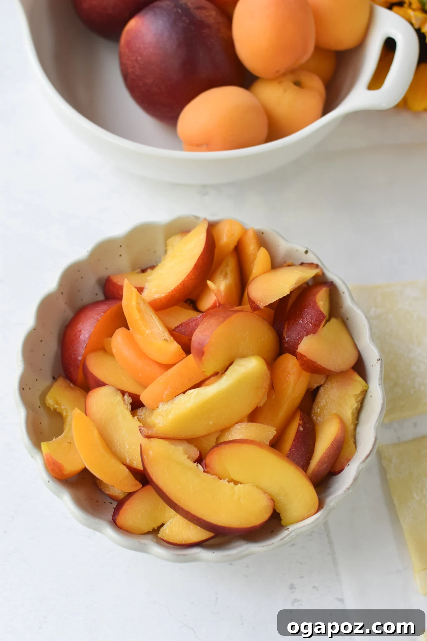 Effortless Golden Peach Tart 6 A bowl filled with thinly sliced nectarines, ready to be arranged on the puff pastry. The slices are uniform and vibrant.