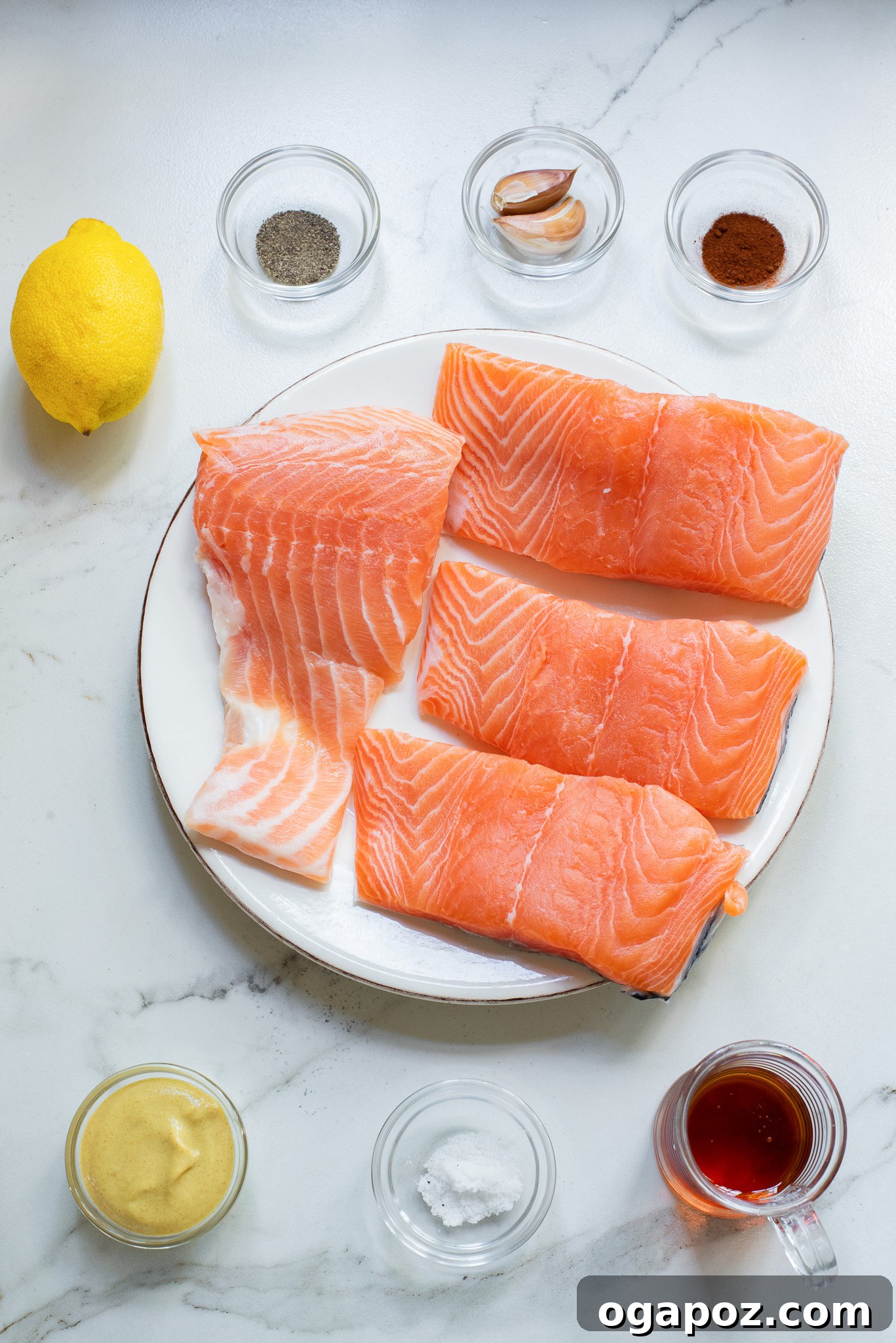 A flat lay showing all ingredients for Honey Mustard Salmon: salmon fillets, honey, Dijon mustard, lemon, paprika, cayenne pepper, garlic, salt, and pepper.