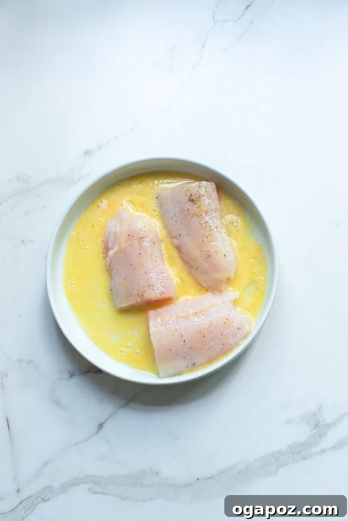 One-Pan Fish Perfection 5 Easy Pan-Fried Fish fillet being dipped in beaten egg.