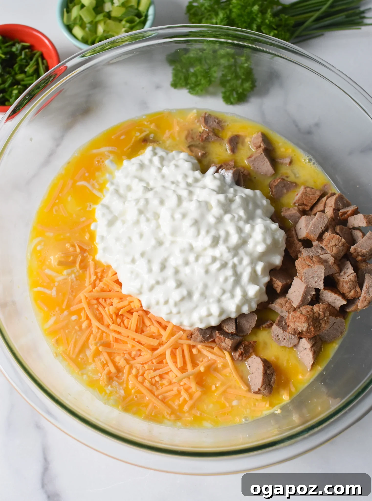 Savory Cottage Cheese Egg Bake 6 All the delicious ingredients for Cottage Cheese Baked Eggs—including cheeses, cooked sausage, and aromatic herbs—have been added to the whisked eggs in a large mixing bowl, ready for stirring.