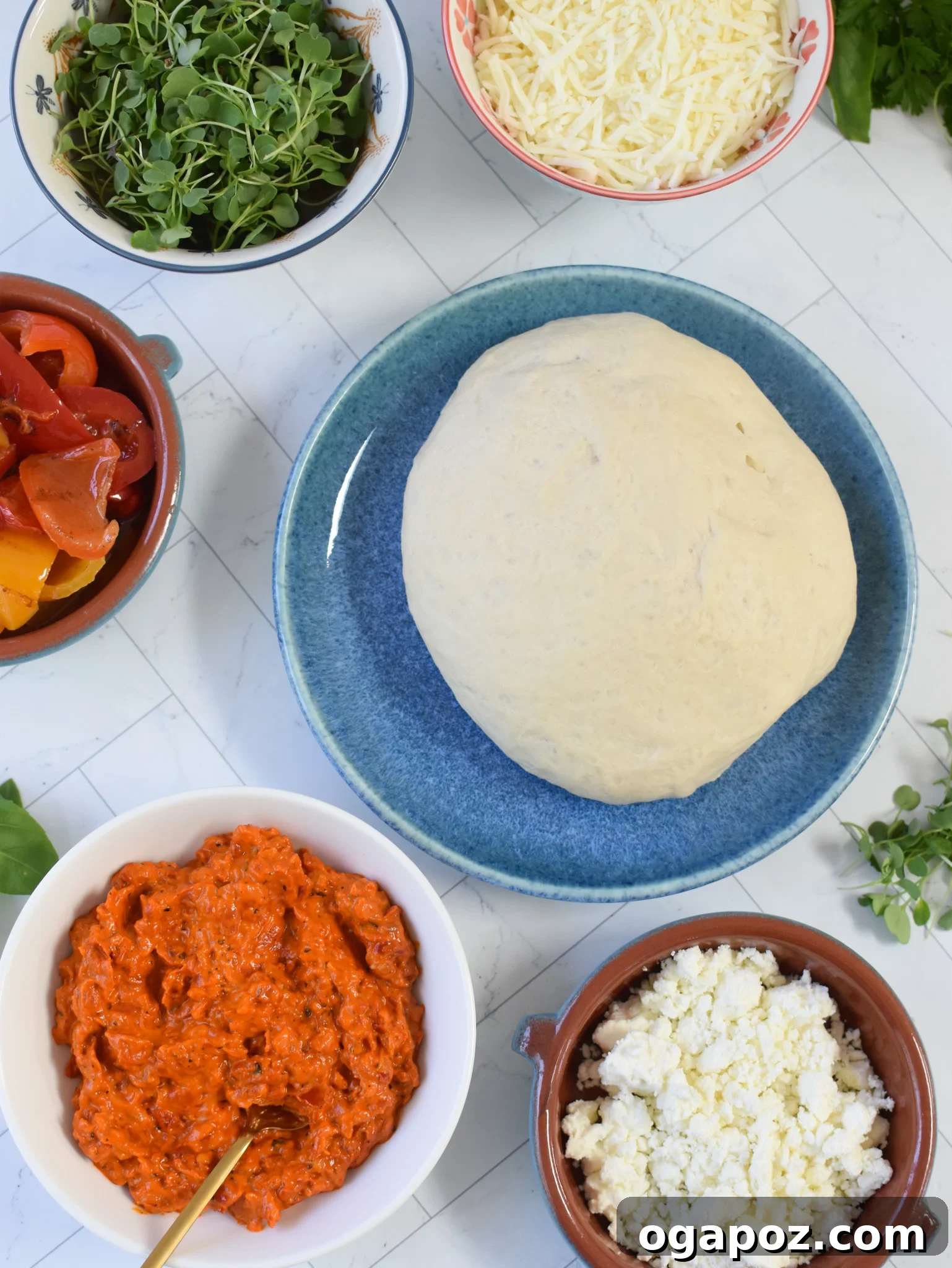 Sun-Kissed Mediterranean Skillet Pizza 6 A selection of fresh, vibrant ingredients for Cast Iron Mediterranean Pizza, including dough, red pepper spread, cheese, and herbs.