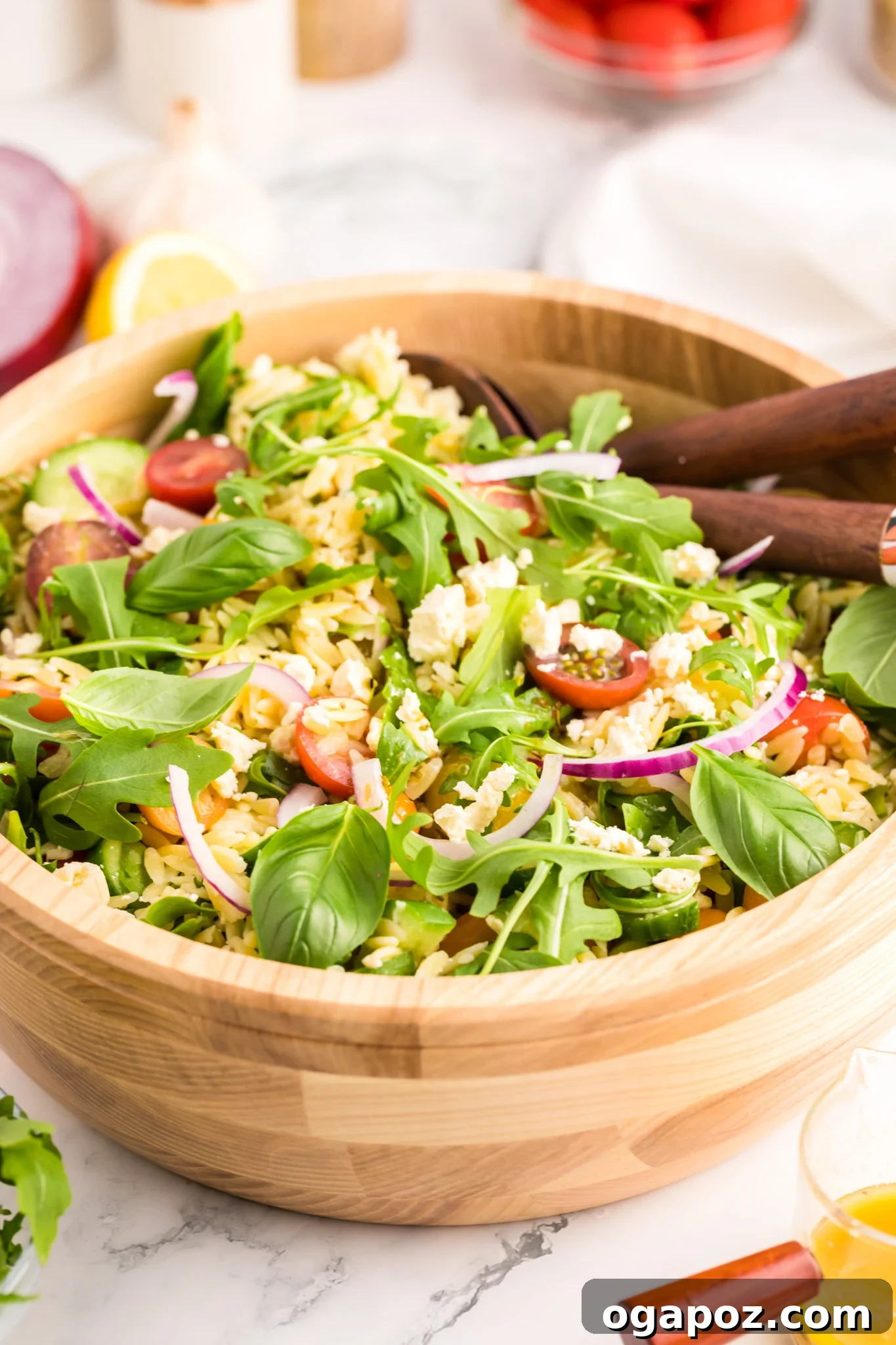 Vibrant Arugula Orzo Salad 2 Arugula Orzo Salad in a white bowl with wooden spoons, showcasing fresh ingredients.