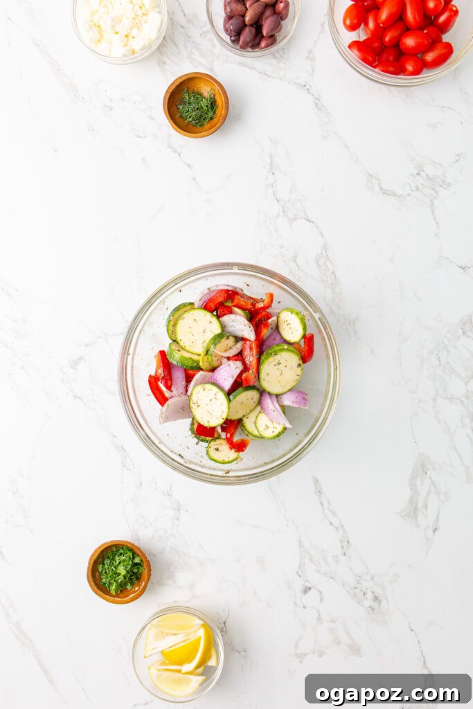 Zesty Mediterranean Sheet Pan Chicken 8 Mixed vegetables (red onion, bell pepper, zucchini) in a bowl with marinade.
