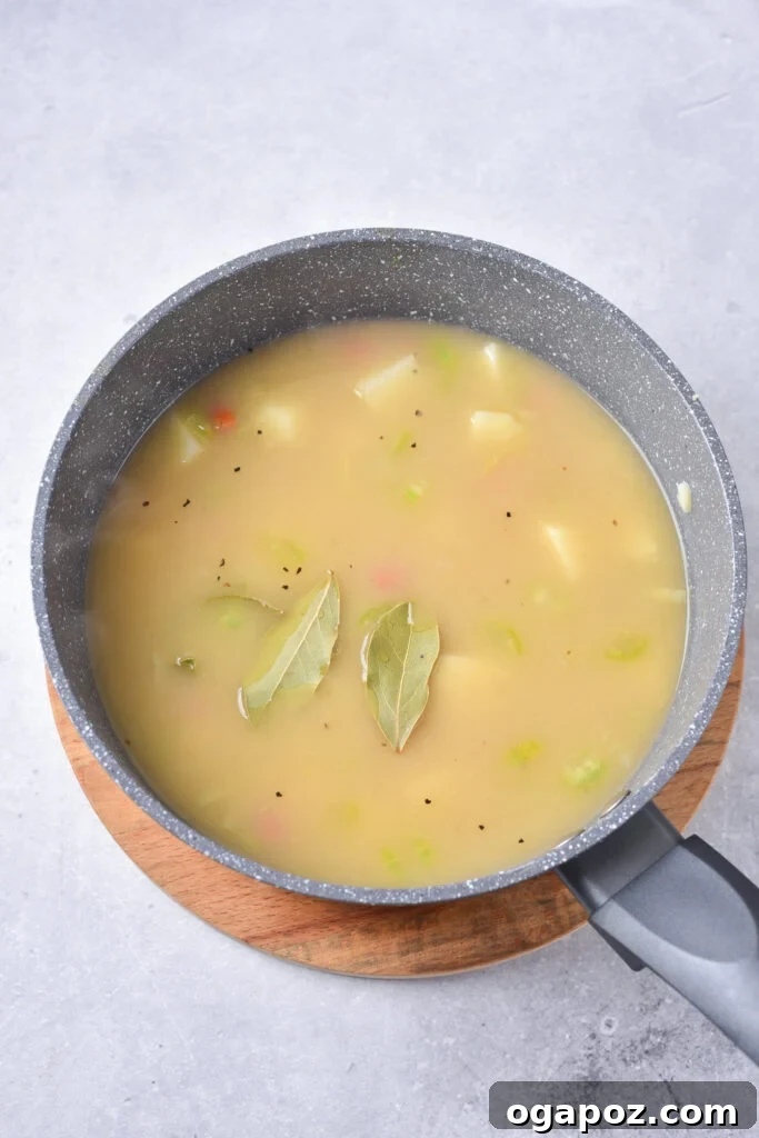 Velvety Potato Leek Soup 8 Potato Leek Soup simmering in a pot with a bay leaf visible, indicating the cooking process.
