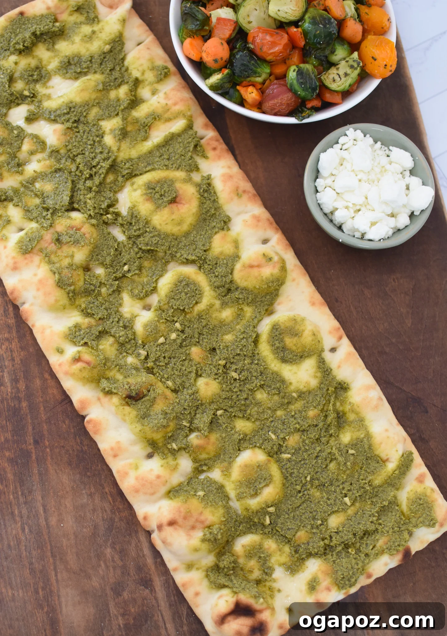 Gourmet Goat Cheese and Roasted Vegetable Flatbread 10 Flatbread crusts on a baking sheet, spread with a vibrant layer of green pesto.
