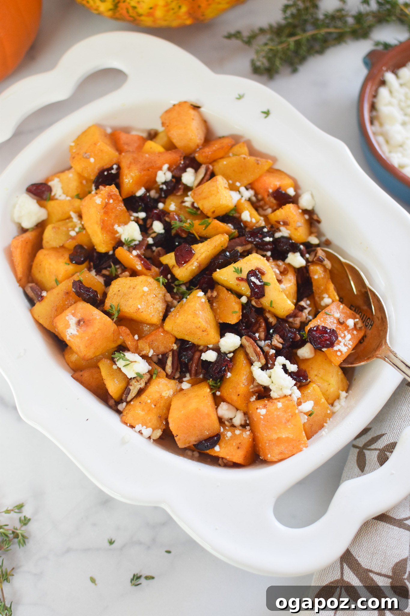 Roasted Butternut Squash with Cranberries being served from a white bowl with a spoon.