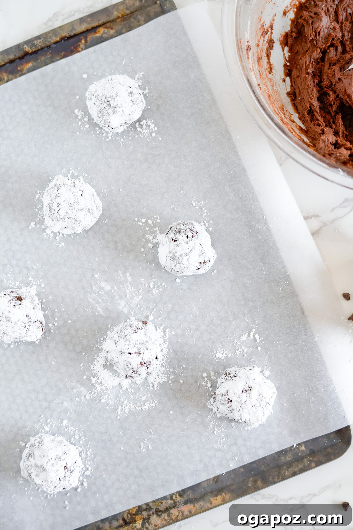 Decadent Chocolate Crinkle Cookies 11 Chocolate Crinkle Cookie Recipe dough balls on a baking sheet, coated in powdered sugar and spaced for baking.