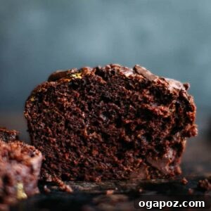 A perfectly baked chocolate zucchini muffin, cut in half to showcase its incredibly moist texture and the generous distribution of dark chocolate chips within.