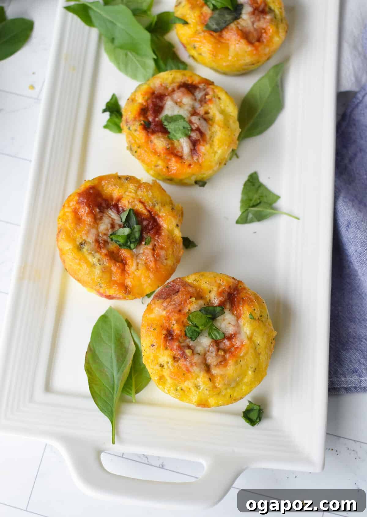 Savory Pizza Egg Cups 3 Appetizing Pizza Egg Muffins arranged neatly on a pristine white platter, garnished with fresh basil leaves, ready to be enjoyed.