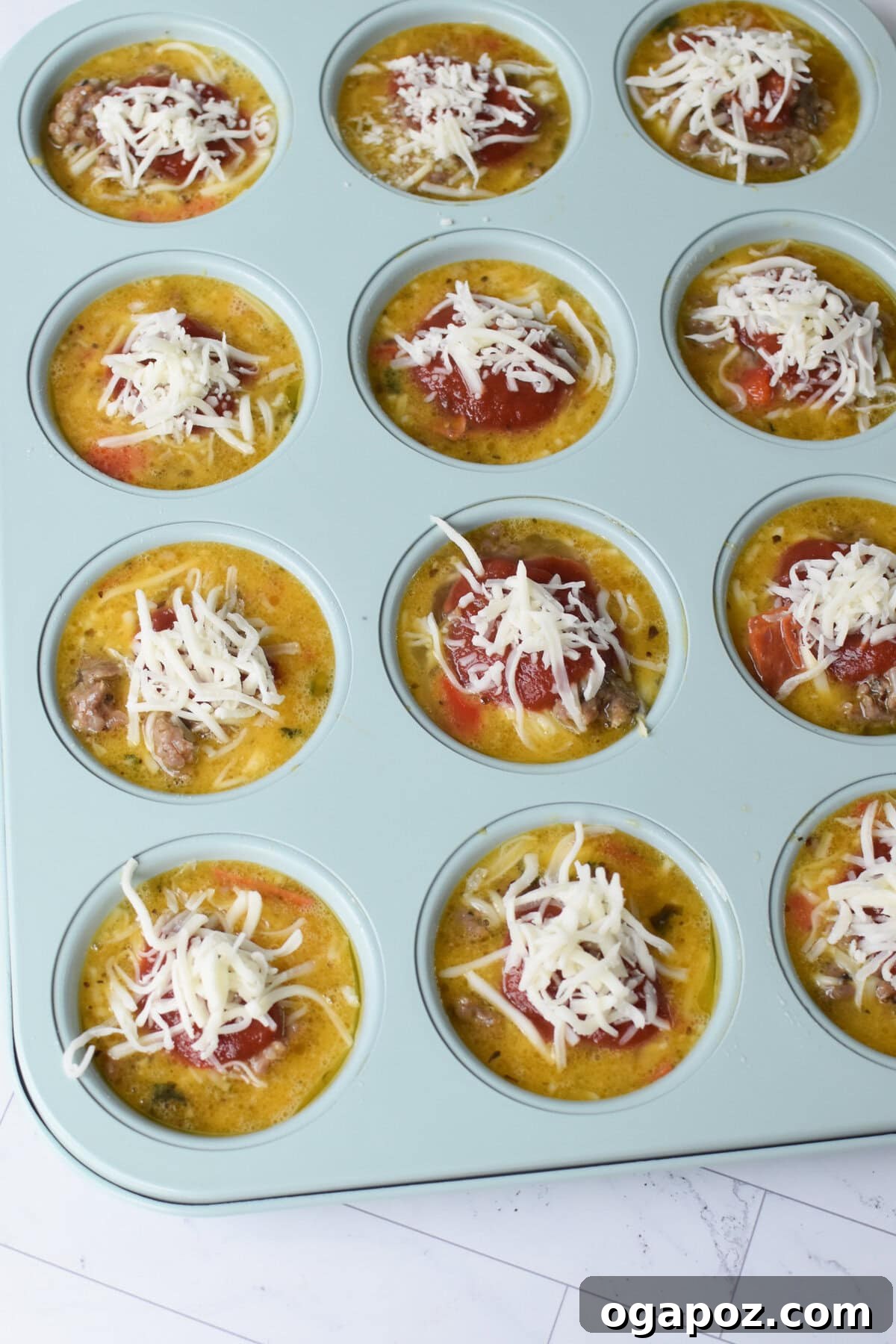 Savory Pizza Egg Cups 8 Unbaked Pizza Egg Muffins nestled in muffin tins, topped with sauce and cheese, patiently waiting to be baked to golden perfection.