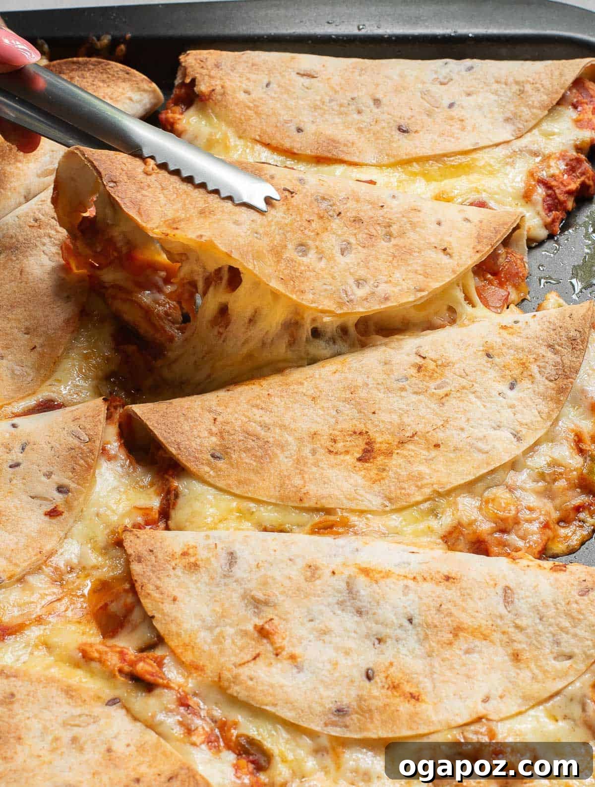 Serving tongs lifting a golden baked chicken taco from a tray, highlighting its crispy texture