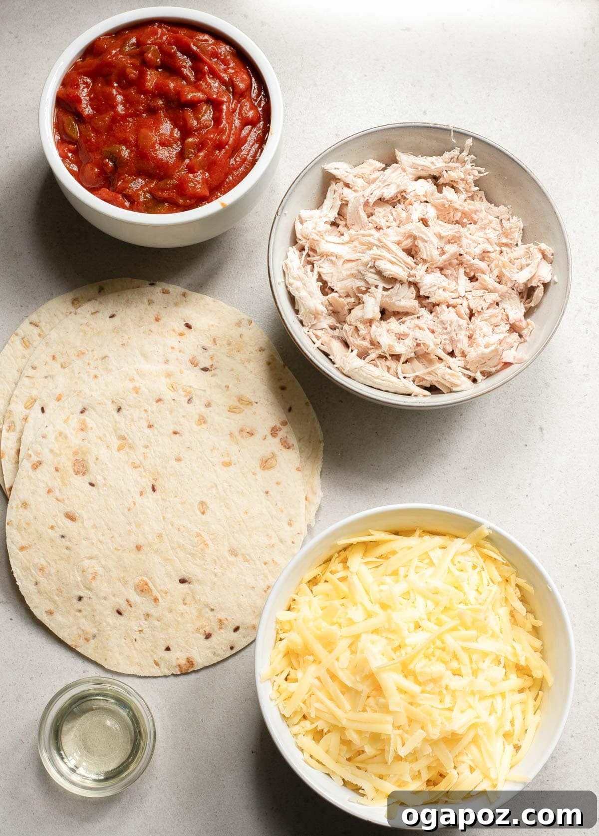 A selection of fresh ingredients for baked chicken tacos laid out: shredded chicken, salsa, spices, tortillas, and cheese