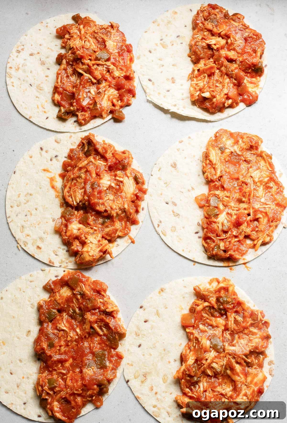 Chicken and cheese mixture spread on one half of a tortilla, ready to be folded for baking