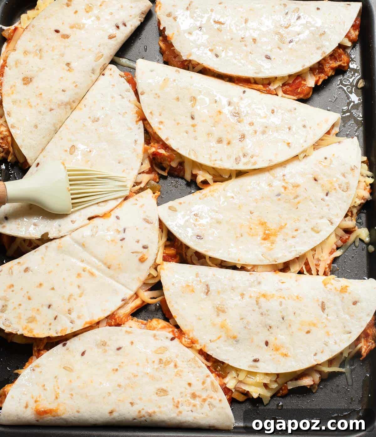 A full baking sheet of neatly folded baked chicken tacos, ready for baking