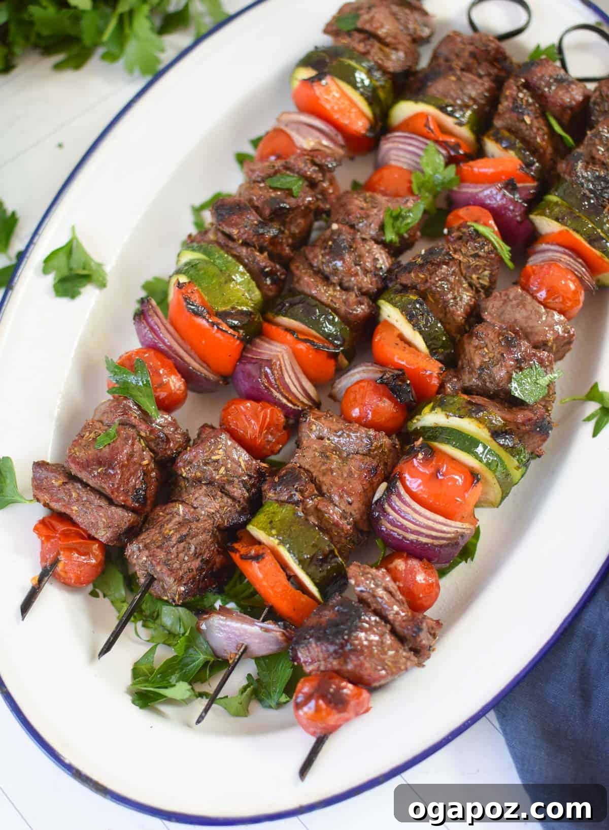 Grilled Beef Souvlaki Skewers 6 Grilled Beef Souvlaki skewers resting on a white platter.