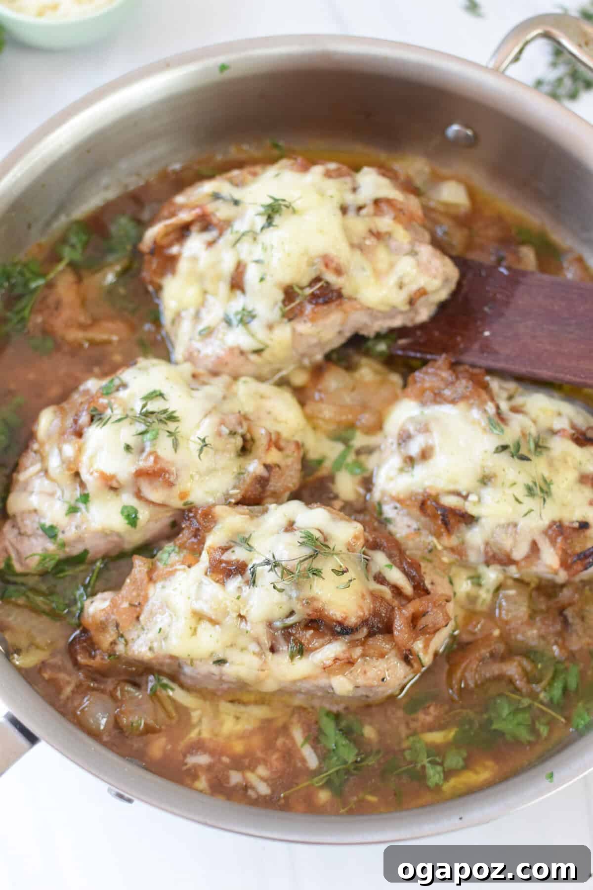French Onion Pork Chops in a skillet, gently lifted with a wooden spatula to show the rich sauce.