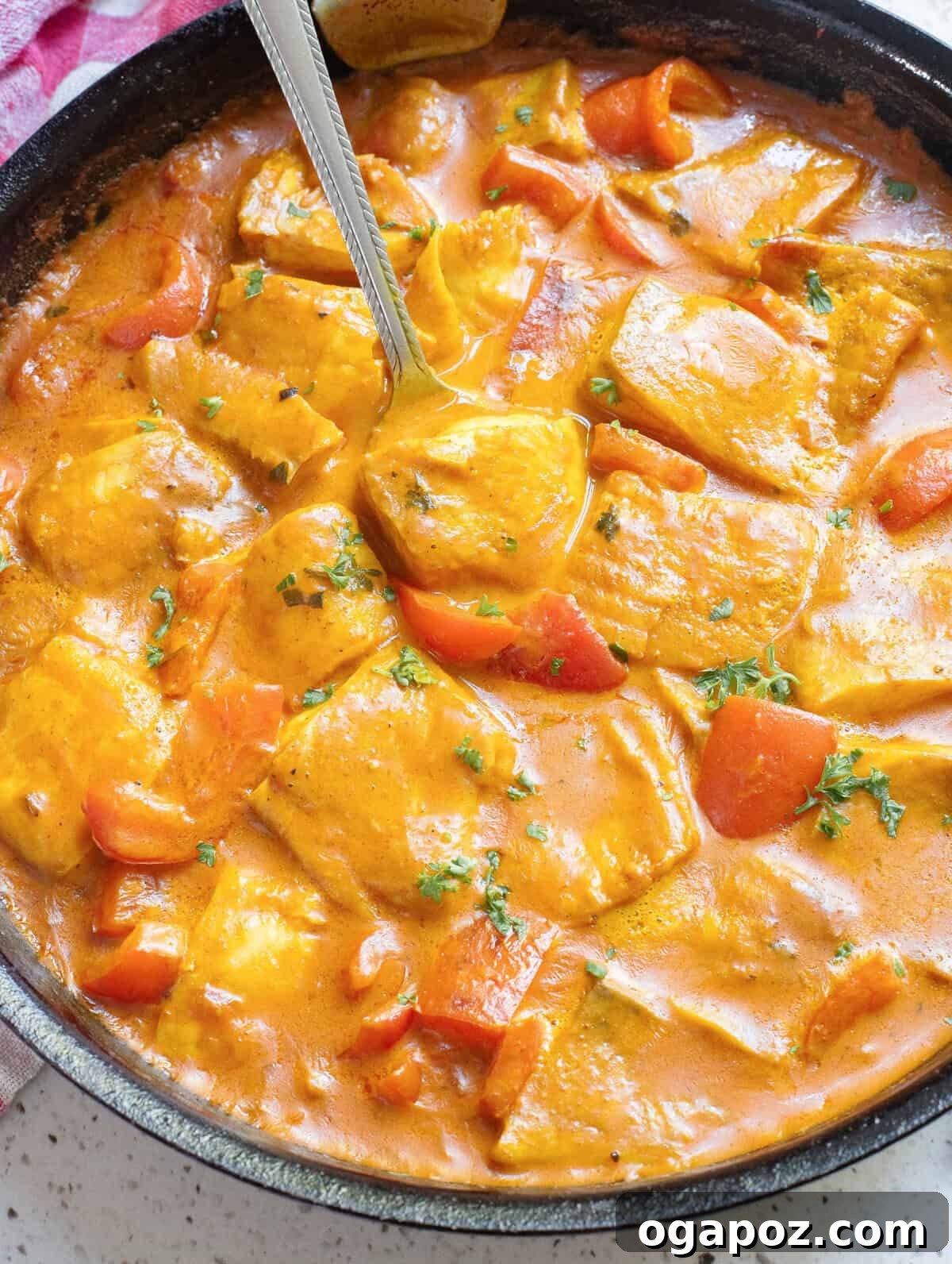 A vibrant Coconut Fish Curry bubbling in a large skillet, ready to be served, with a spoon resting in it.