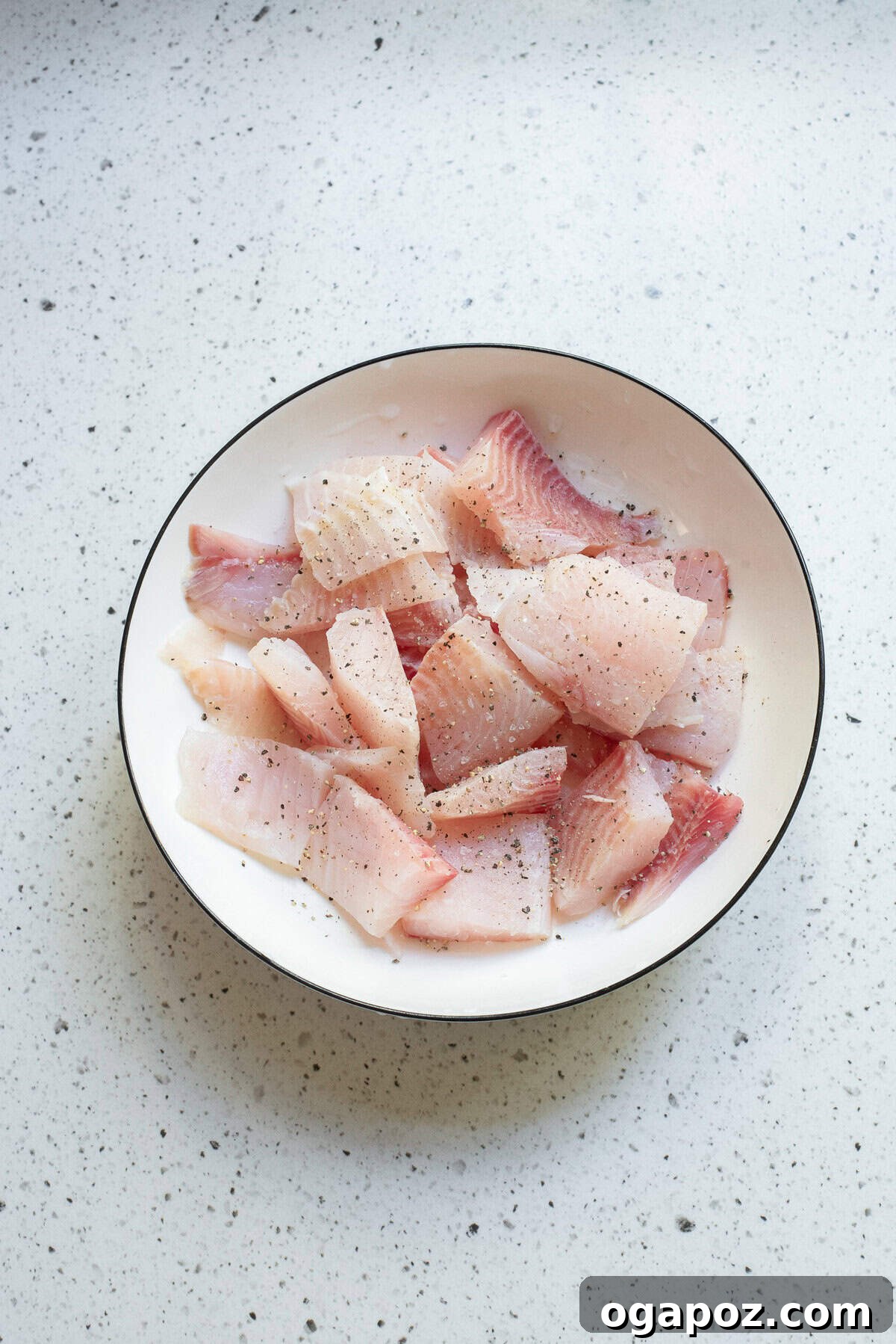 Seasoned raw white fish fillets cut into pieces in a white bowl, ready for cooking in the curry.