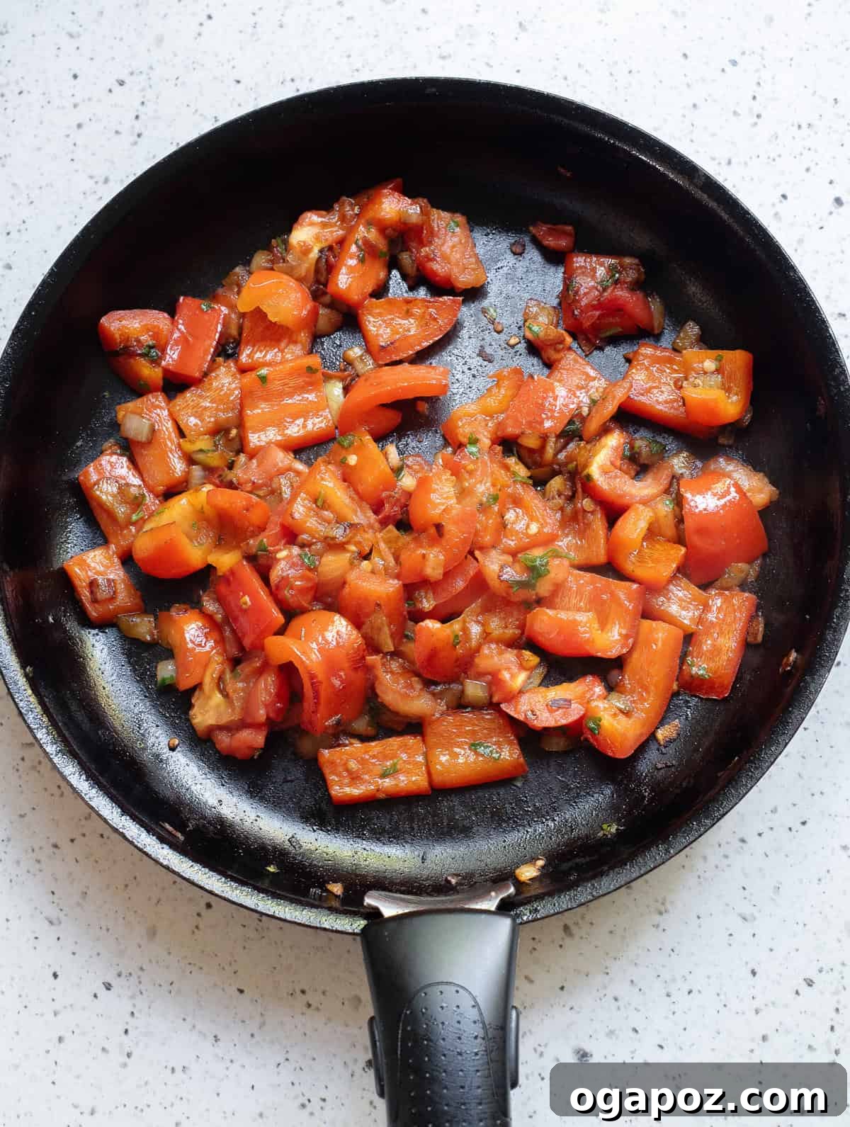 A colorful mixture of sautéed vegetables, including onions, bell peppers, and tomatoes, simmering in a skillet, forming the base of the fish curry.