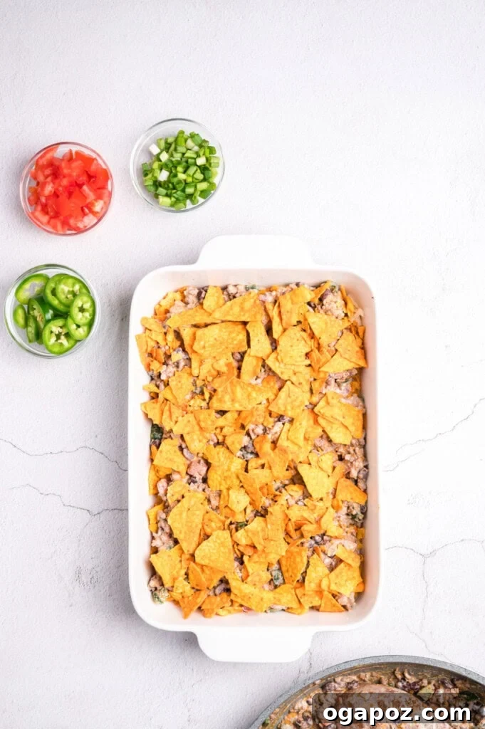 Doritos chips being layered onto the beef mixture in a baking dish