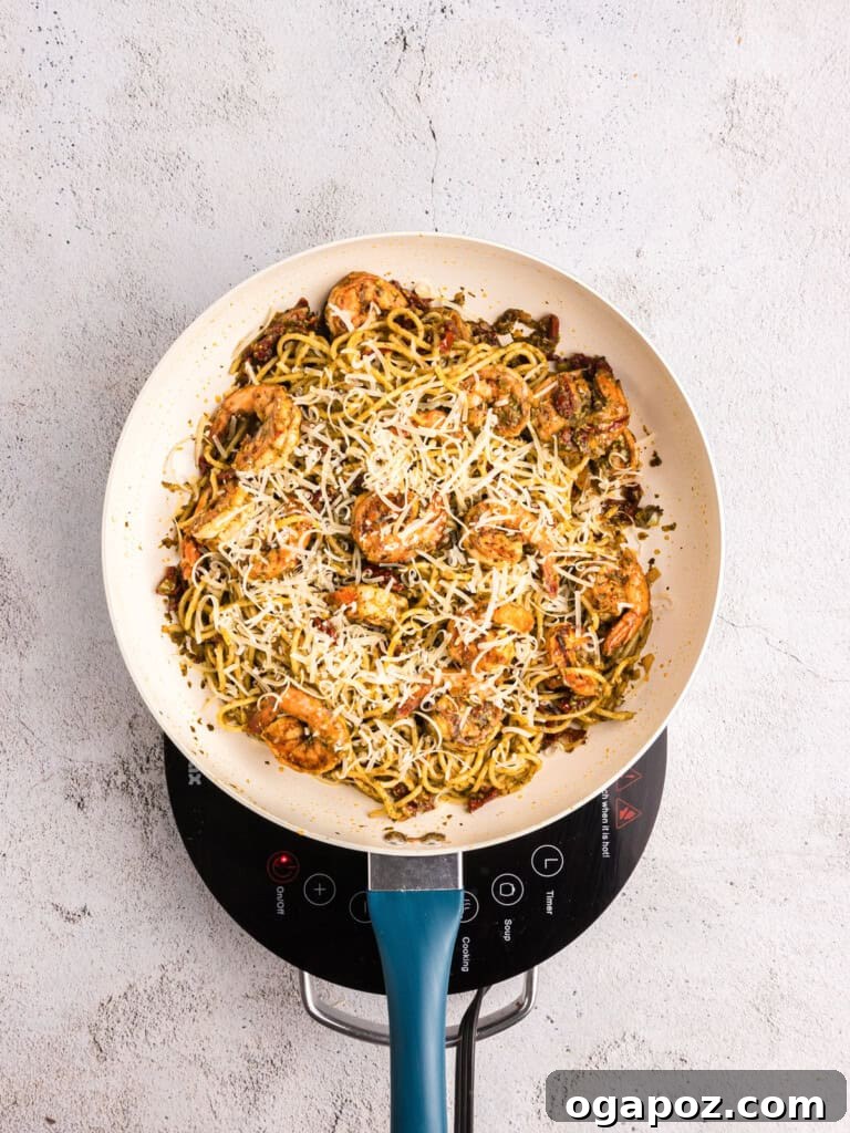 Vibrant Pesto Shrimp Pasta 10 Cooked pasta, sun-dried tomatoes, and cheese being added to the shrimp mixture in a pan