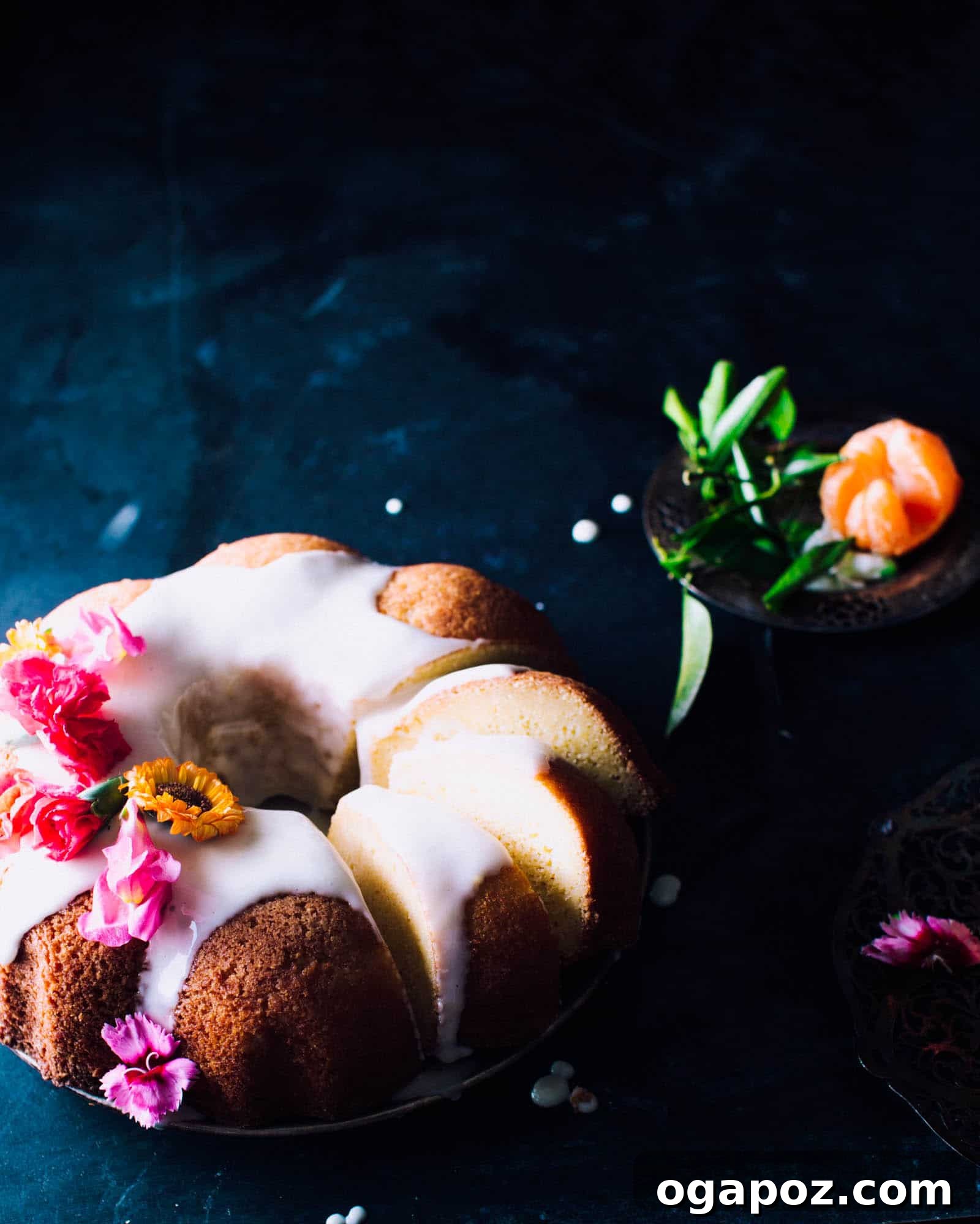 Vibrant orange pound cake with generous orange icing and delicate flowers, ready to be served on a pristine white surface