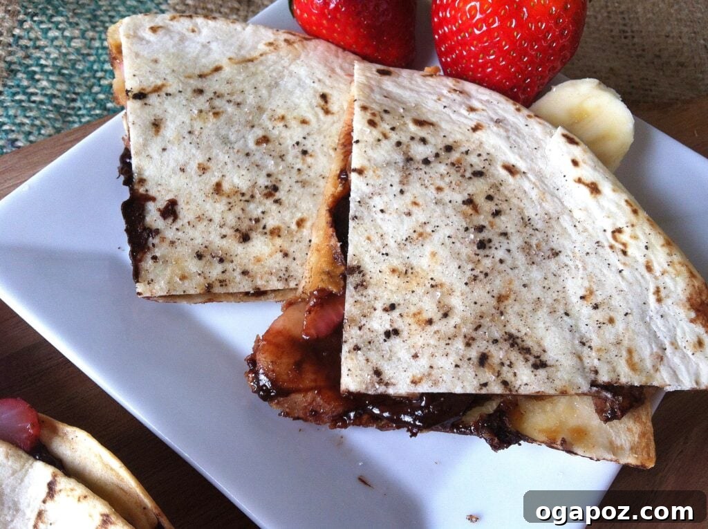 Heavenly Sweet Quesadillas 2 Golden-brown Dessert Quesadilla sliced on a white plate, showcasing melted chocolate, bananas, and strawberries spilling out.