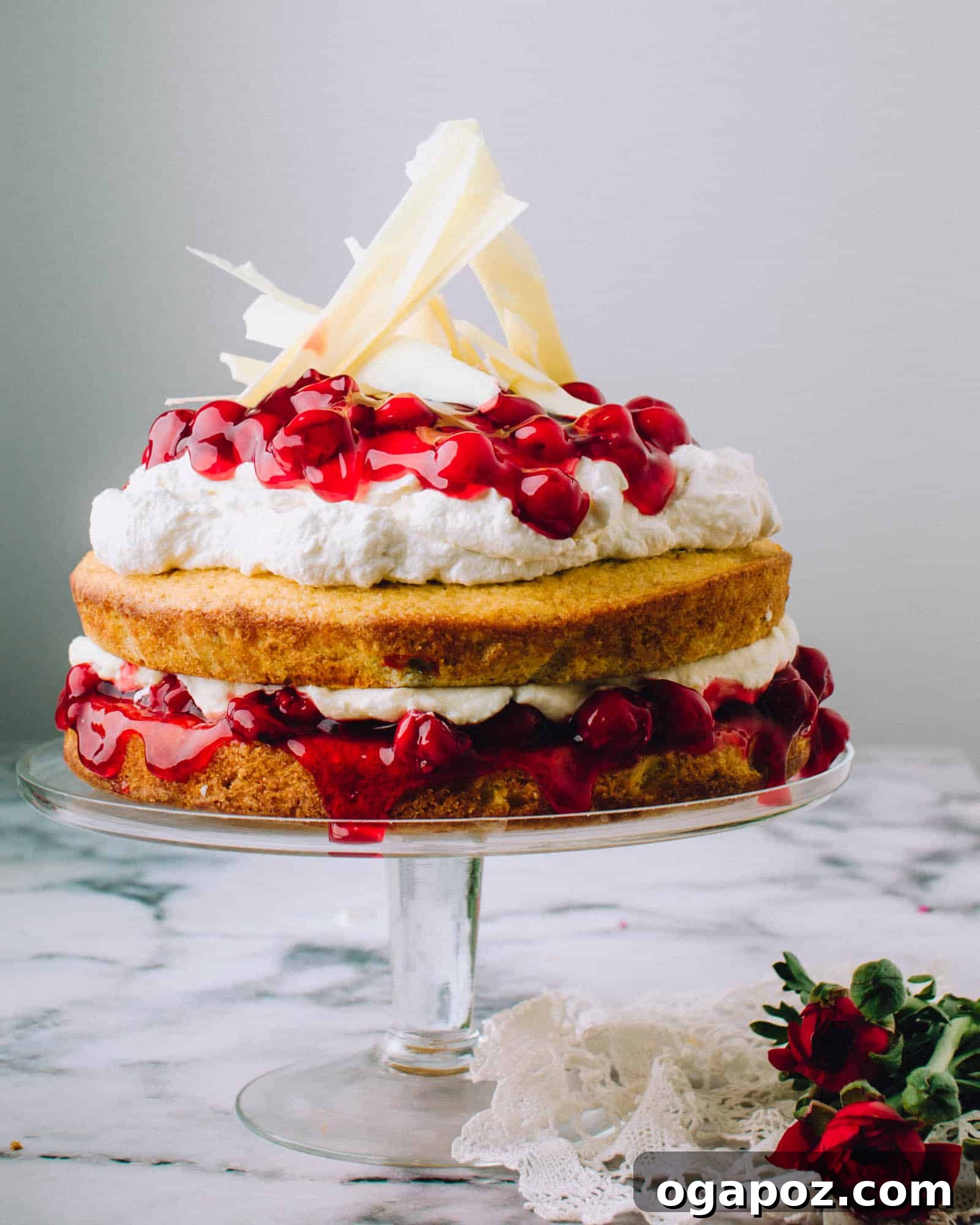 Pristine Cherry Delight 2 A beautifully decorated White Chocolate Cherry Cake, showcasing layers of moist vanilla cake, rich white chocolate mousse, and vibrant cherry pie filling, topped with whipped cream and delicate white chocolate shards.