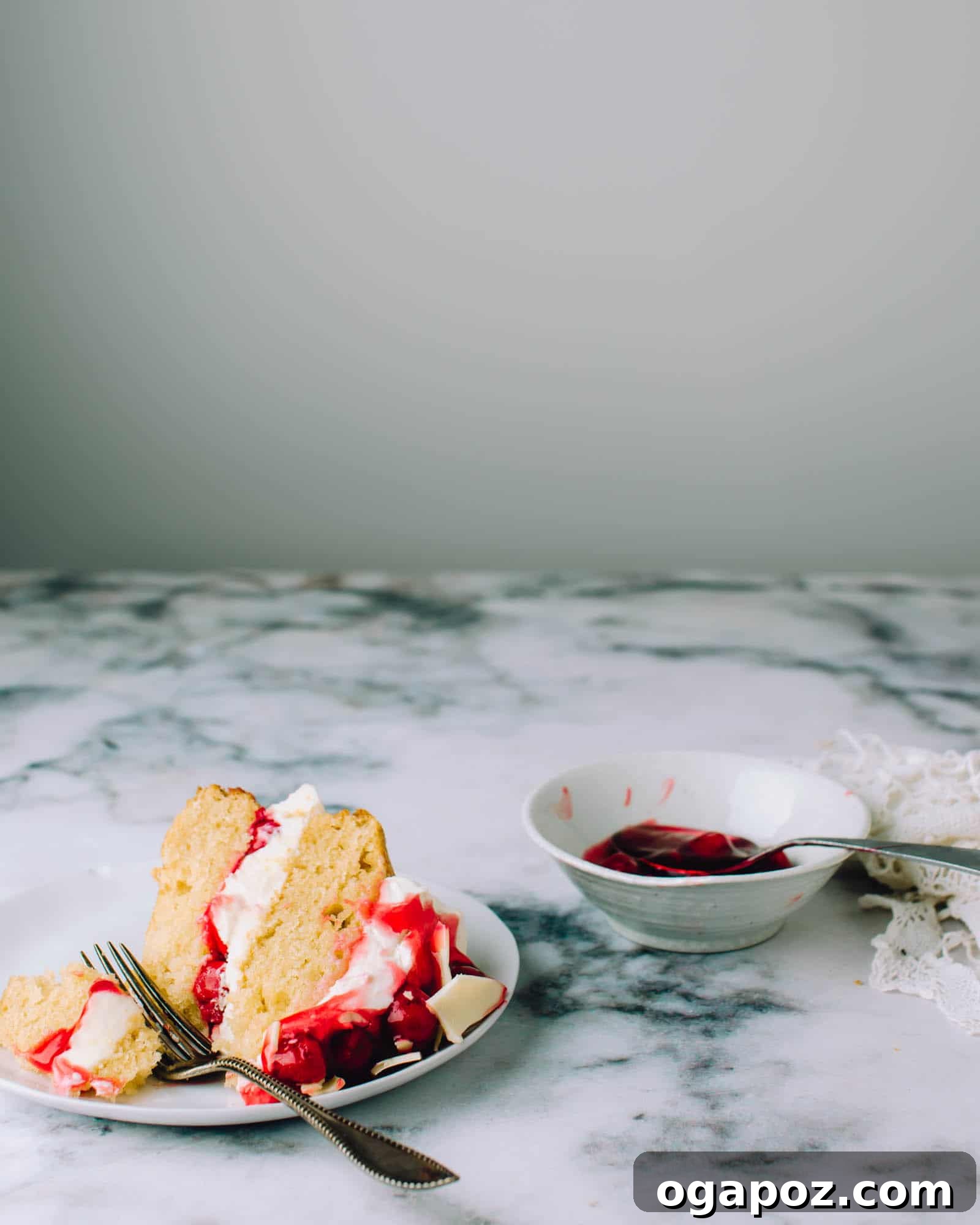 Pristine Cherry Delight 7 A full, tall White Chocolate Cherry Cake presented on a beautiful cake stand, elegantly garnished with fresh cherries and homemade white chocolate shards, ready to be served and enjoyed.