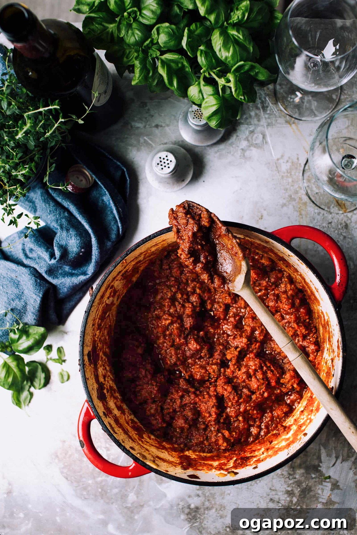 Effortlessly Decadent Meat Sauce 2 A big pot of rich, simmering meat sauce with fresh herbs, ready to be served over pasta, with a blue napkin nearby.