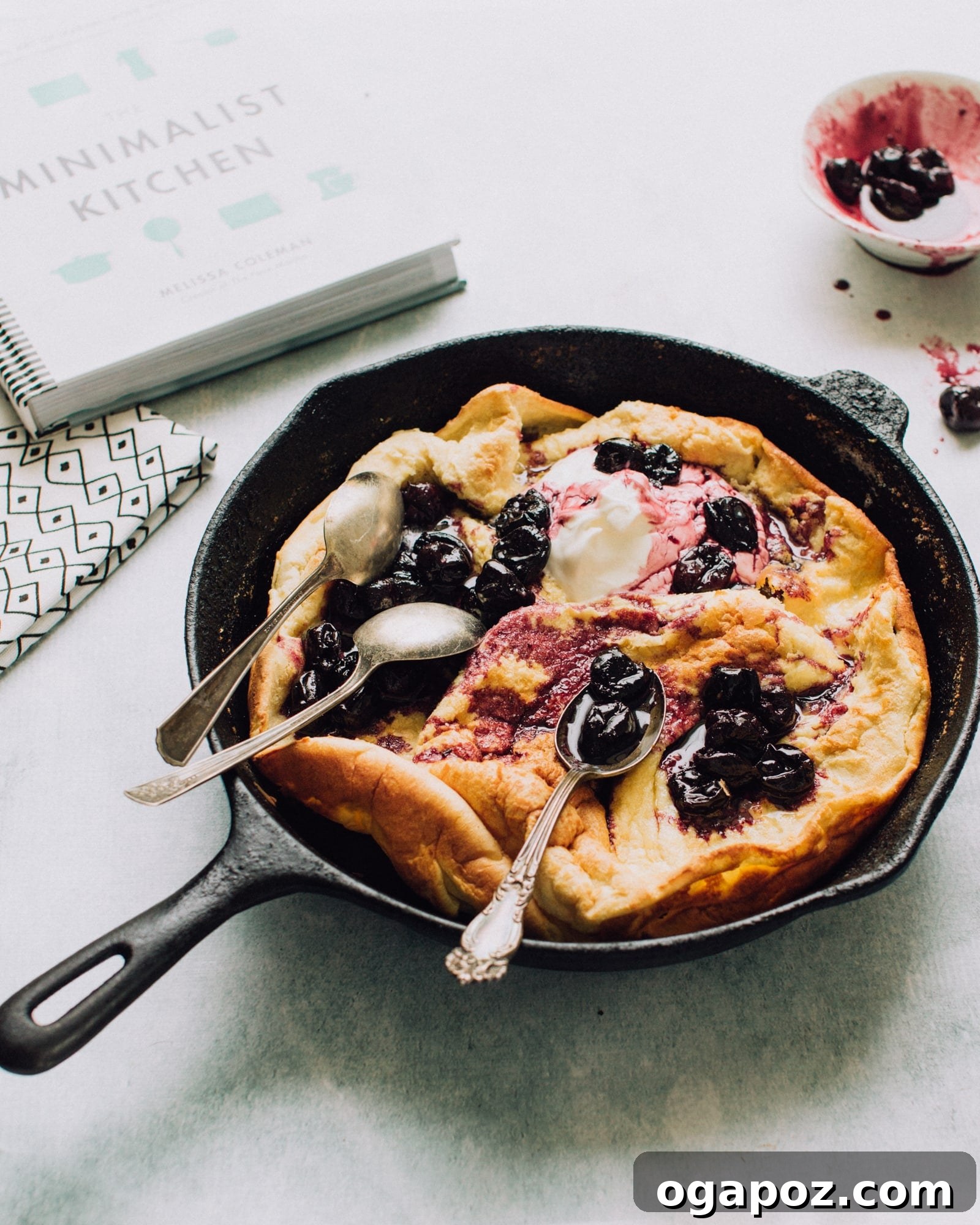 Effortless Blender Puff Pancake 2 Blender Dutch Baby, a golden, puffy pancake served in a cast iron skillet with a cherry topping