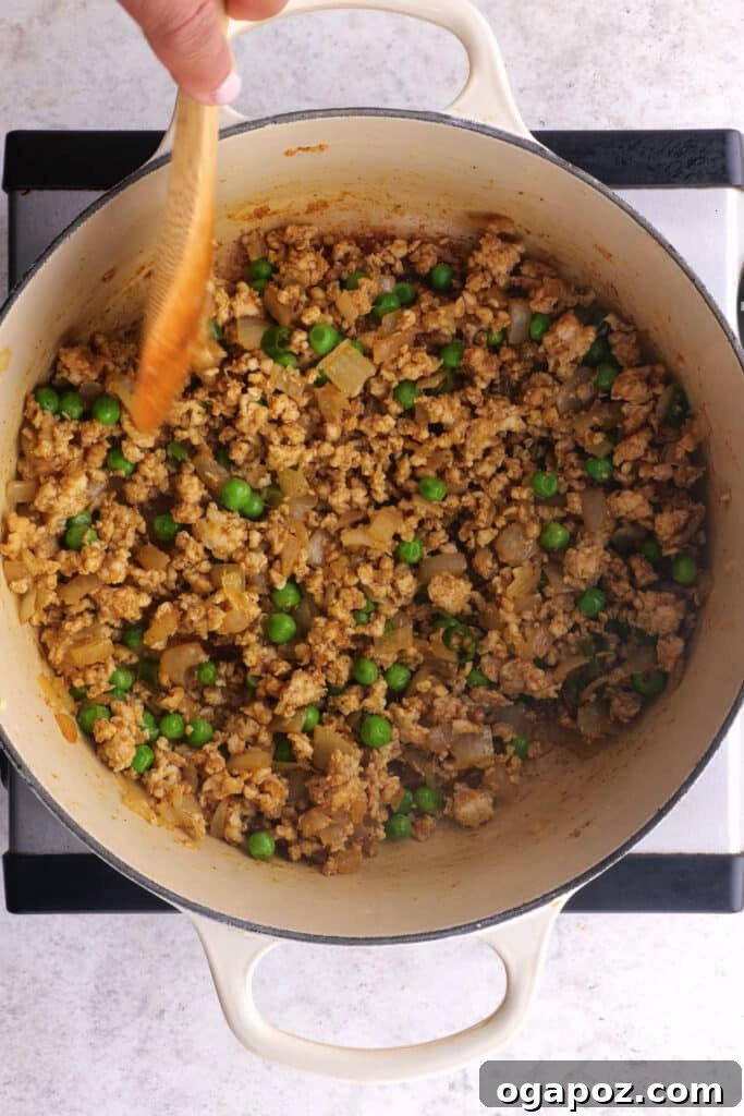 Chicken samosa filling simmering in a large pan with spices and peas.