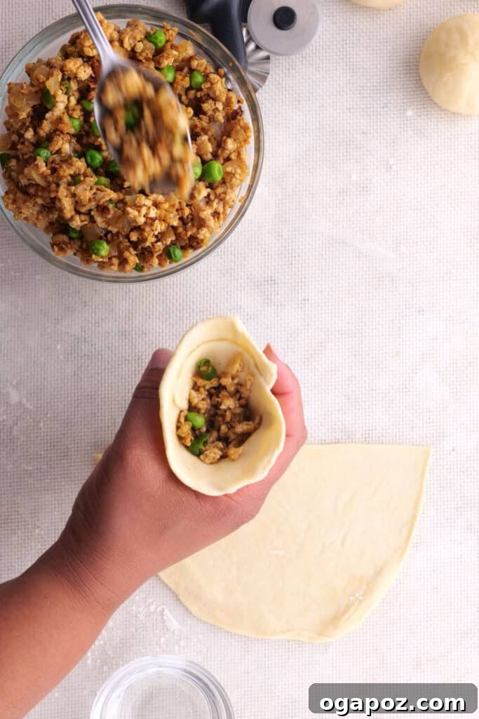 A hand filling a homemade samosa dough cone with the spiced chicken mixture.