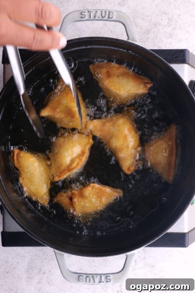 Homemade Chicken Samosas deep frying in hot oil until golden brown.