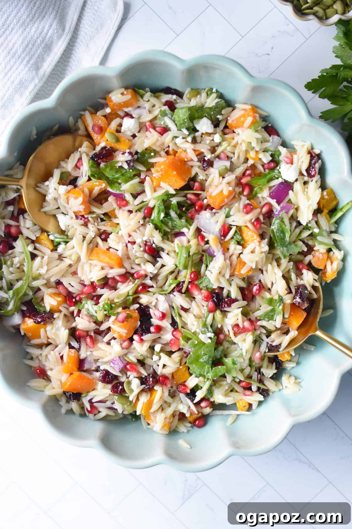 Autumn Harvest Orzo Pasta Salad 7 A large glass bowl overflowing with Fall Orzo Pasta Salad, with elegant serving spoons nestled in, ready for guests.