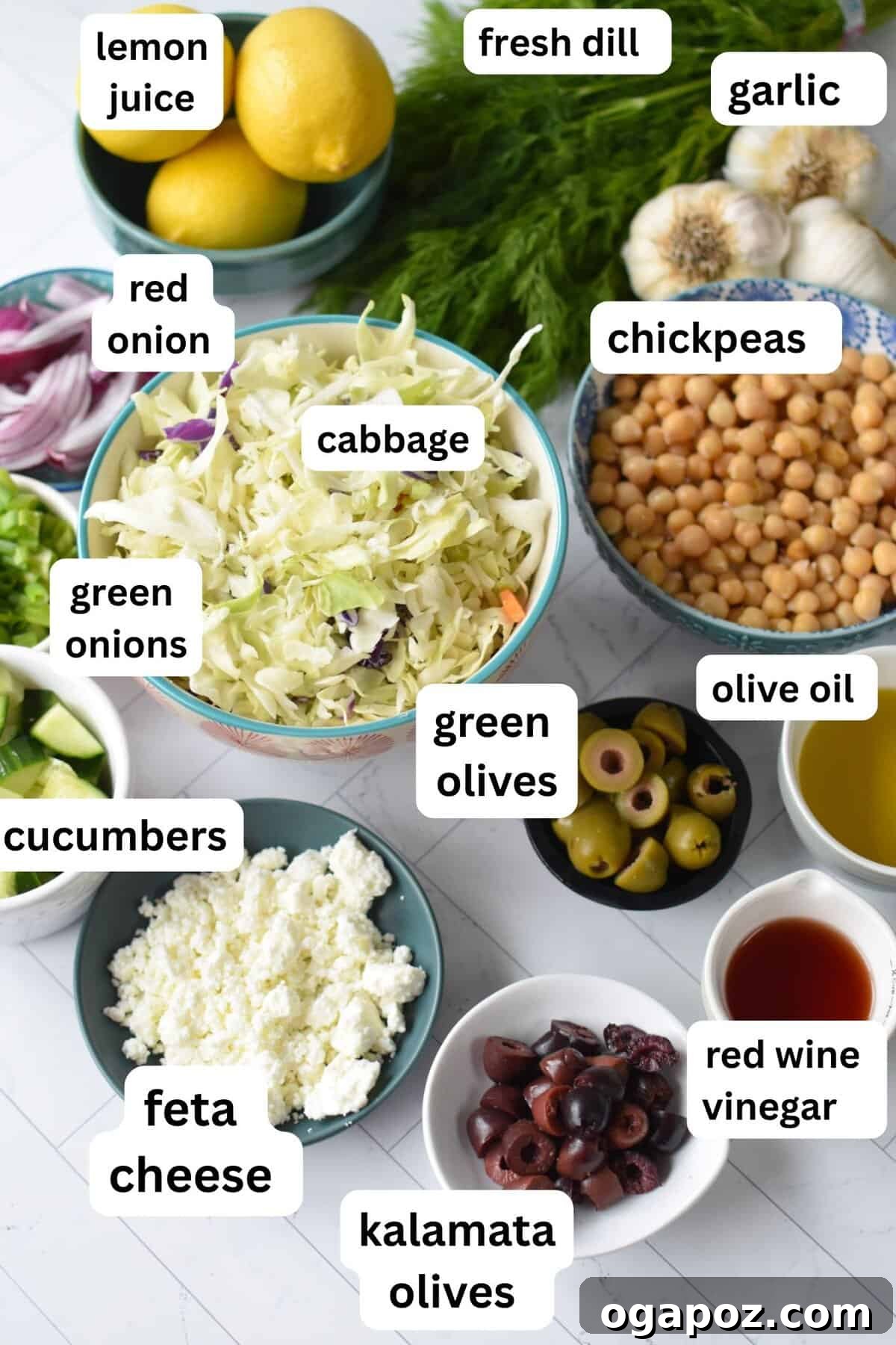 Zesty Greek Cabbage Slaw 5 Individual ingredients for Greek Cabbage Salad laid out attractively on a rustic surface, including shredded cabbage, chickpeas, olives, and fresh herbs.