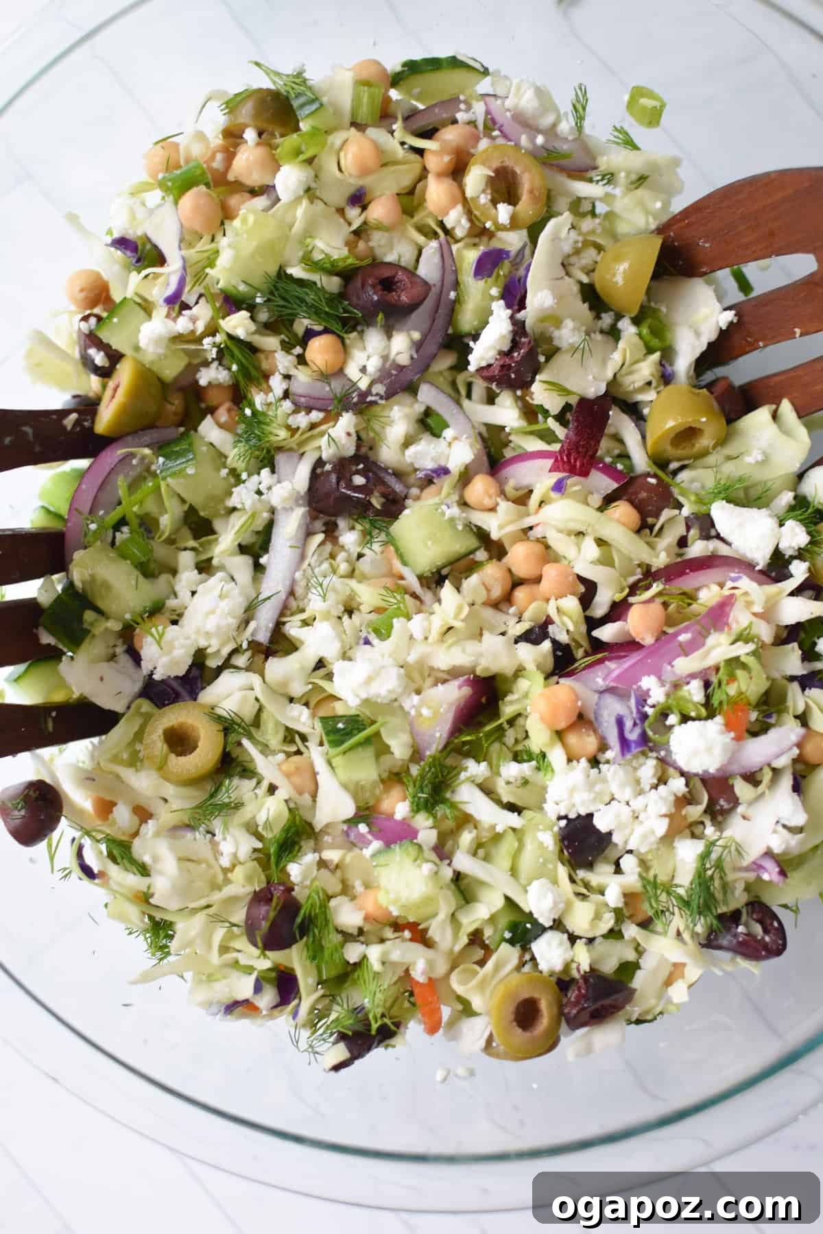 Zesty Greek Cabbage Slaw 6 Greek Cabbage Salad served in an elegant clear glass bowl, accompanied by serving spoons, ready for a gathering.