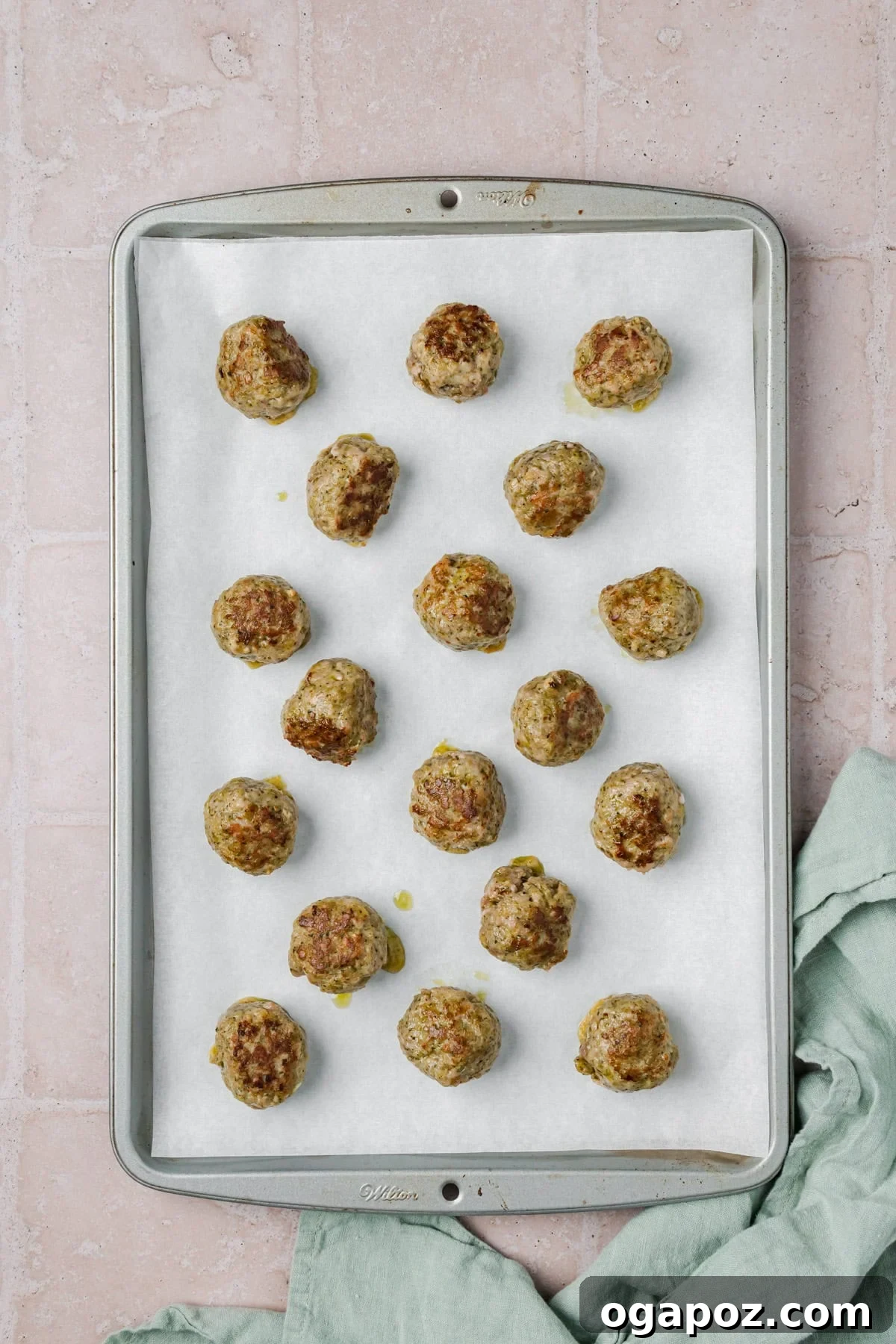 Emerald Pesto Turkey Bites 9 Partially cooked turkey meatballs with vibrant pesto on a baking sheet, arranged and ready for the final cooking stage in the oven.