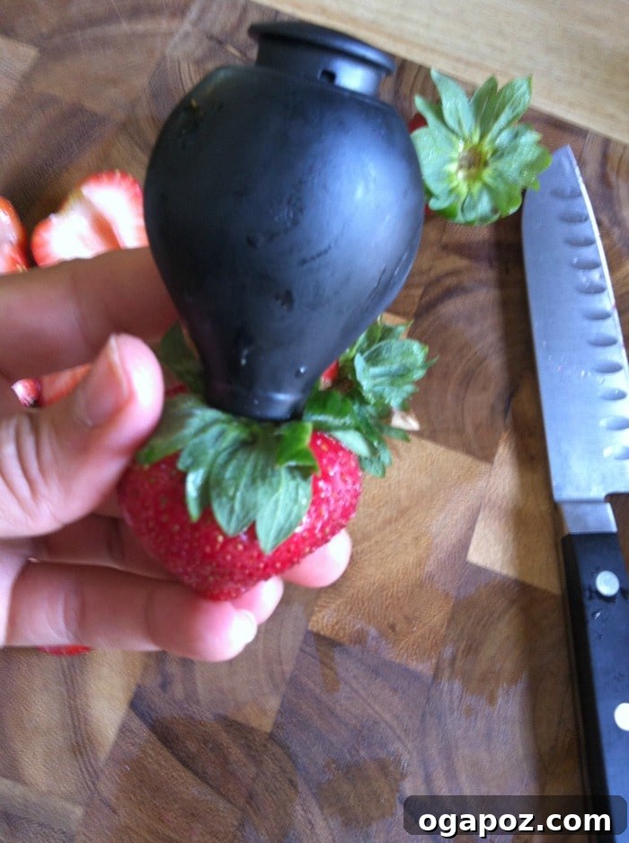 Refreshing Fruit Medley with Zesty Honey-Yogurt Dressing 3 Close-up of the OXO strawberry huller tool in action, perfectly removing the green stem and core from a fresh strawberry, illustrating its ease of use.