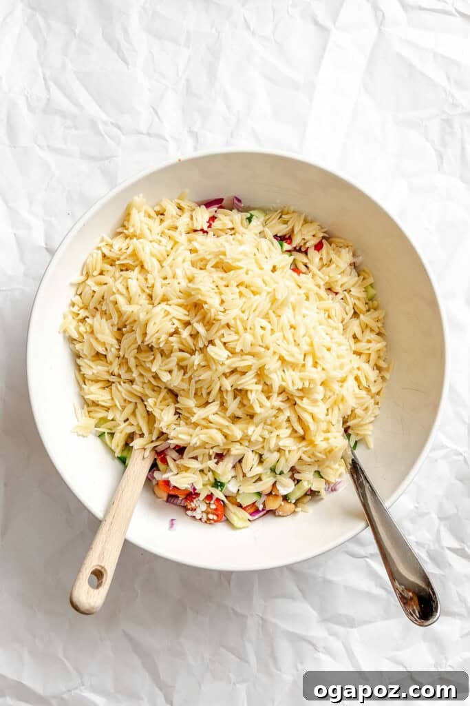 Bright Summer Orzo Salad 10 The cooled orzo pasta being added to the bowl of mixed vegetables and chickpeas.