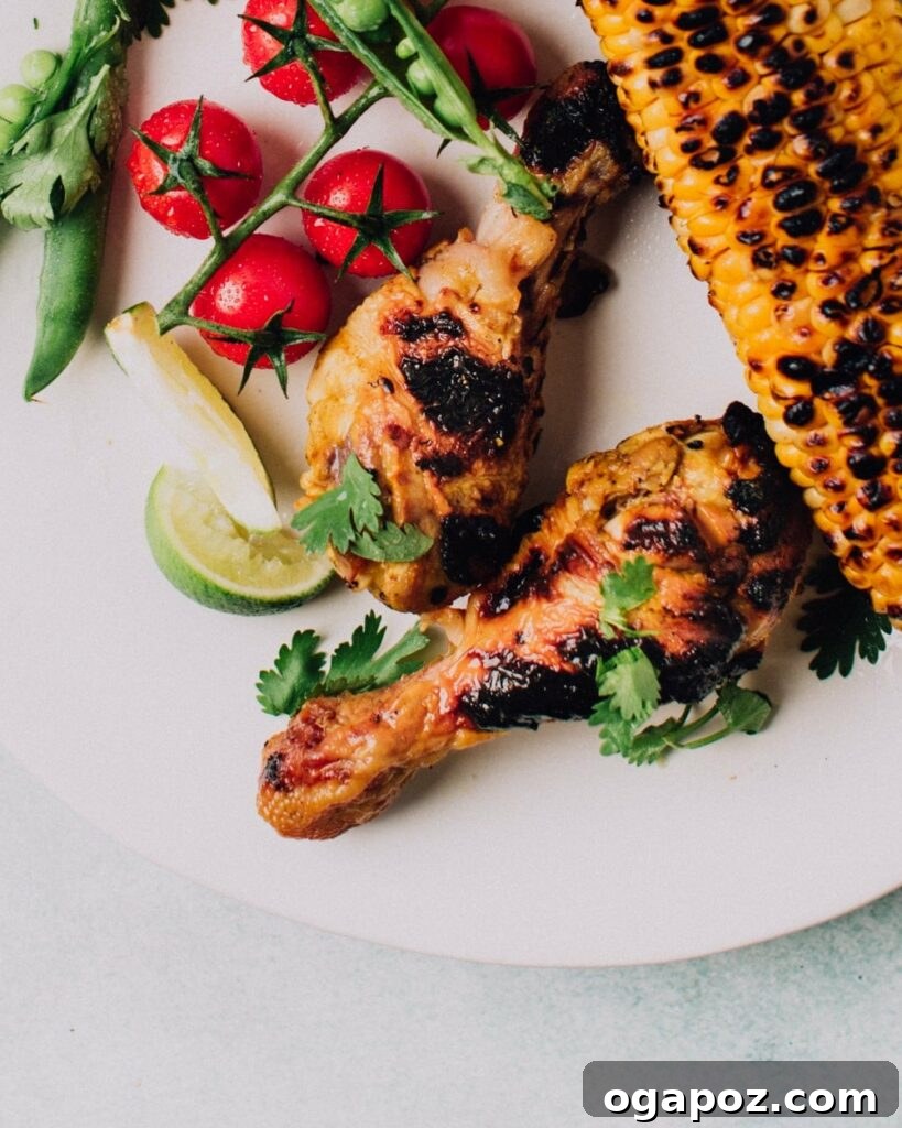 41 Delicious Chicken Drumstick Recipes: Simple and Super Juicy 5 Garlic & Lime Grilled Chicken on a plate with corn cob, baby tomatoes and sliced lime wedges