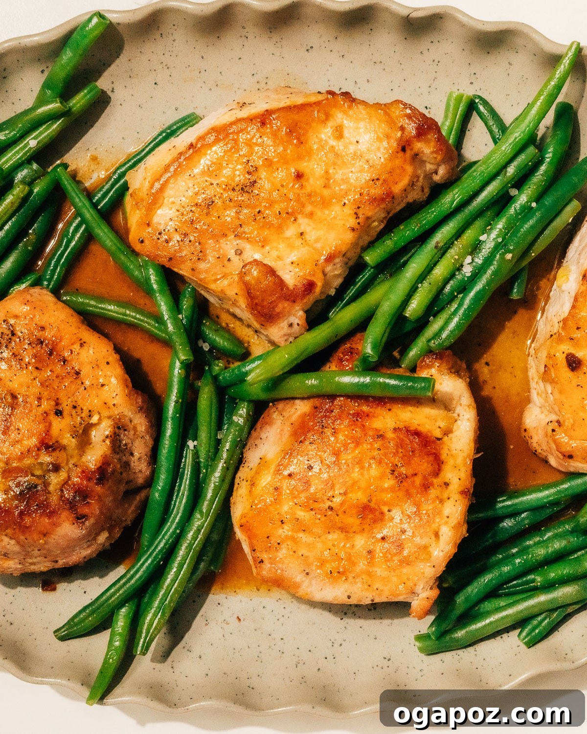 Signature Stuffed Pork Chops with an Unforgettable Pan Sauce 11 Two generous servings of stuffed pork chops, each drizzled with pan sauce, accompanied by vibrant green beans on a white platter, ready to be served.